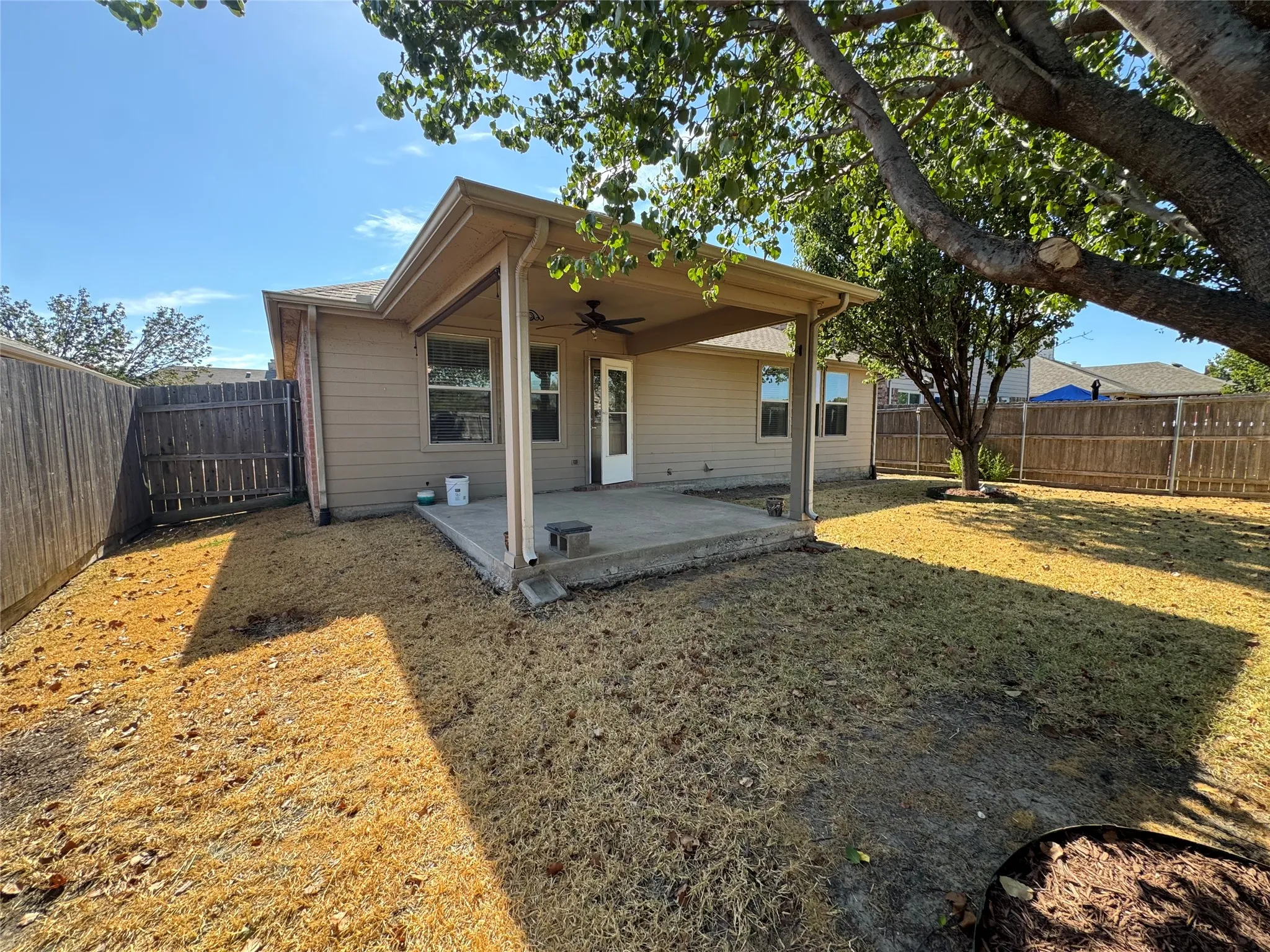 Covered patio with an outdoor ceiling fan, concrete slab, and wood privacy fencing