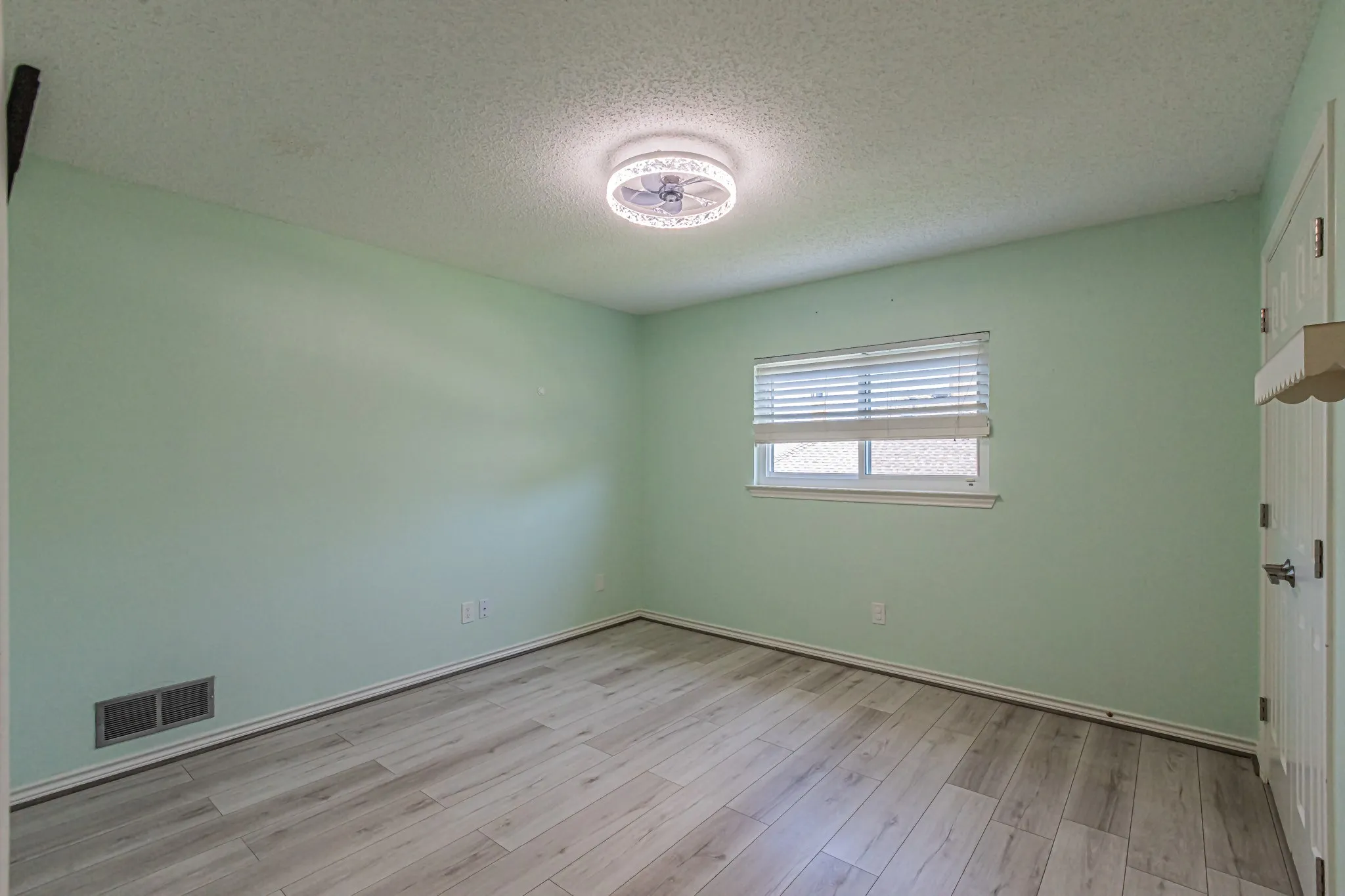 Wood-finish flooring, single window with blinds, ceiling-mounted light fixture, and white trim