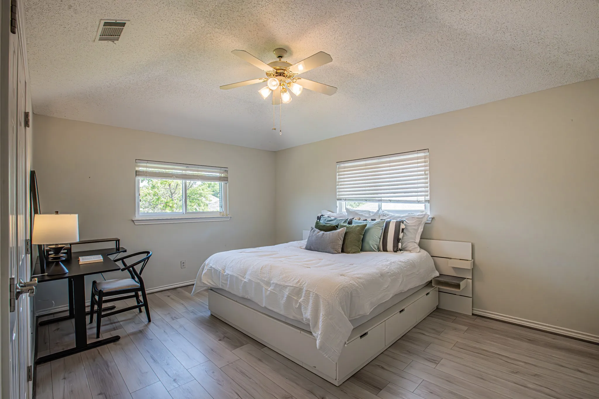 Light-toned wood-finish flooring, two windows with blinds, and a ceiling fan with integrated lighting