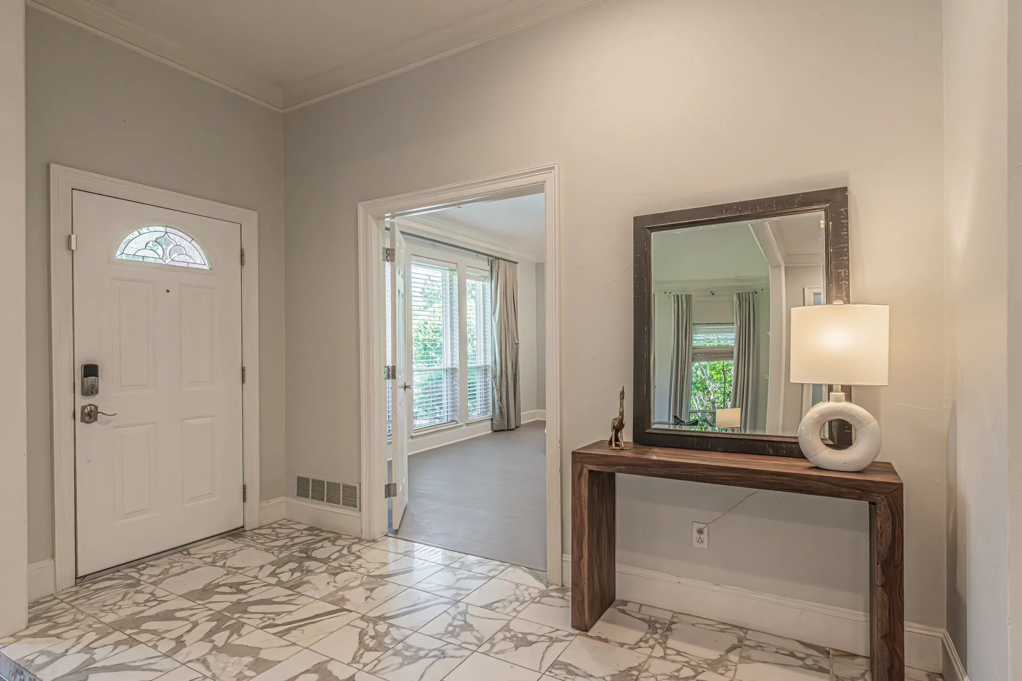 Marble-look tile flooring, white paneled door with leaded glass insert, wood-finish console table, and framed mirror