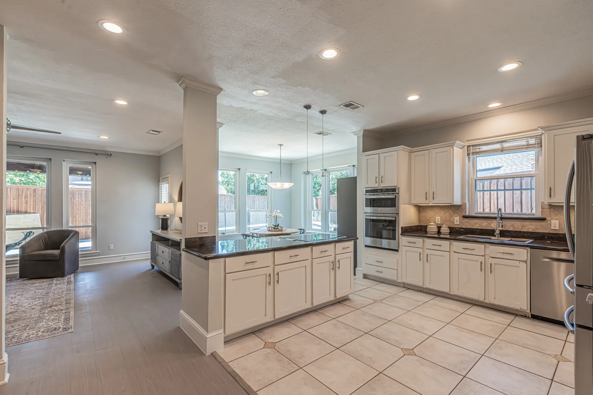 Recessed lighting, tile flooring, built-in double ovens, stainless steel appliances, and a central island with a dark countertop