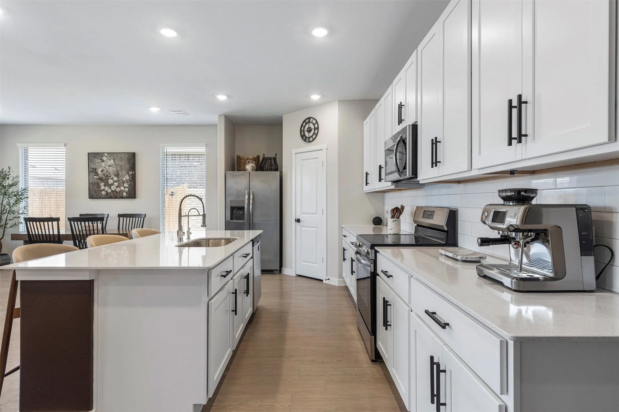Kitchen featuring white cabinetry, stainless steel appliances, a center island with sink, light-toned countertops, and wood-finish flooring