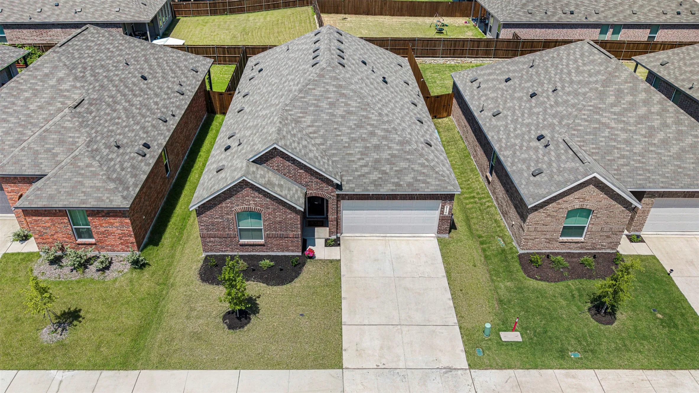 Brick exterior with an attached garage, paved driveway, and manicured front lawn