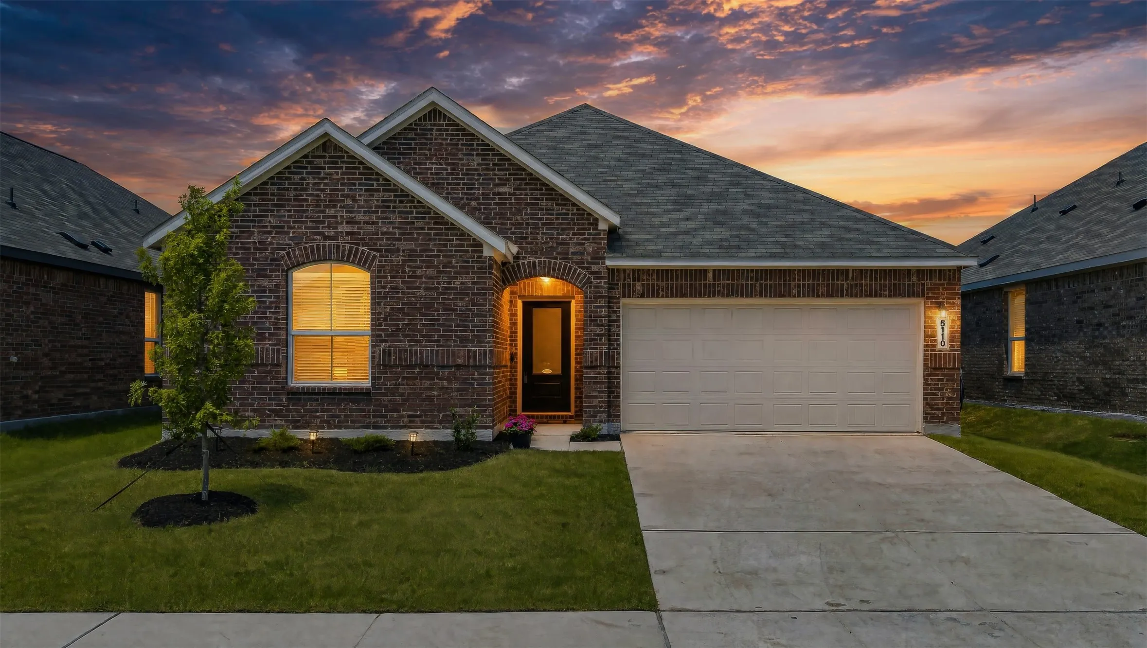 Brick exterior with arched entry, attached garage, concrete driveway, and landscaped front yard