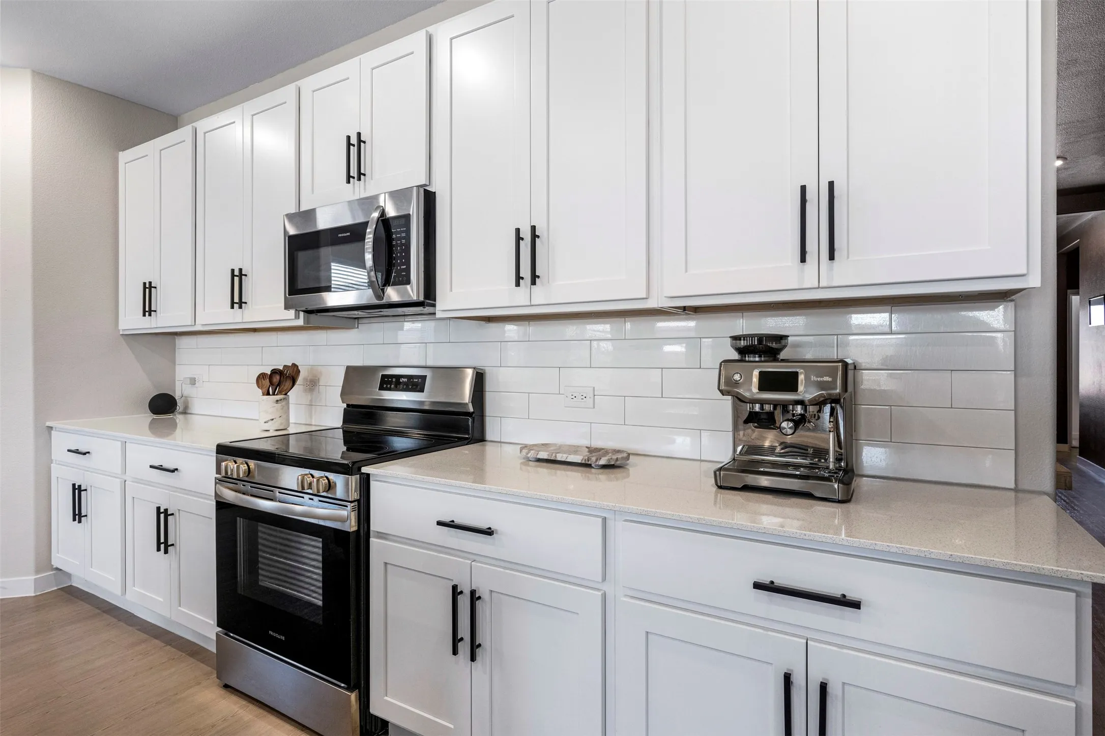 White shaker cabinetry, light-toned countertops, white subway tile backsplash, stainless steel range, and stainless steel microwave