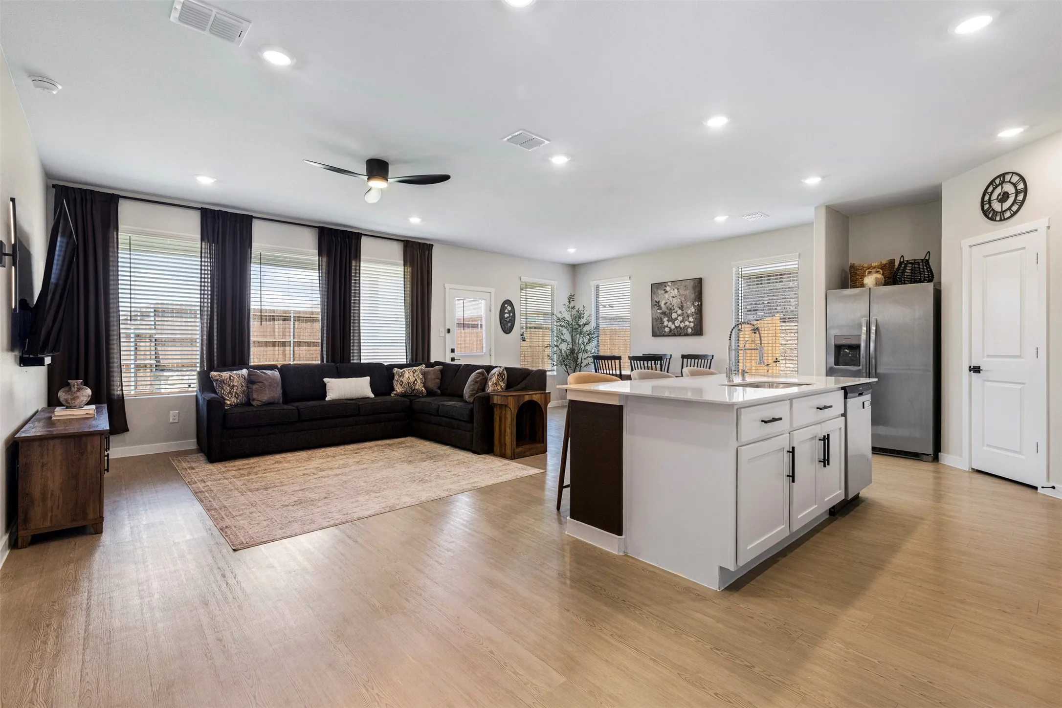 Open-concept living space with wood-finish flooring, recessed lighting, a modern ceiling fan, and a kitchen island featuring white cabinetry and stainless steel appliances