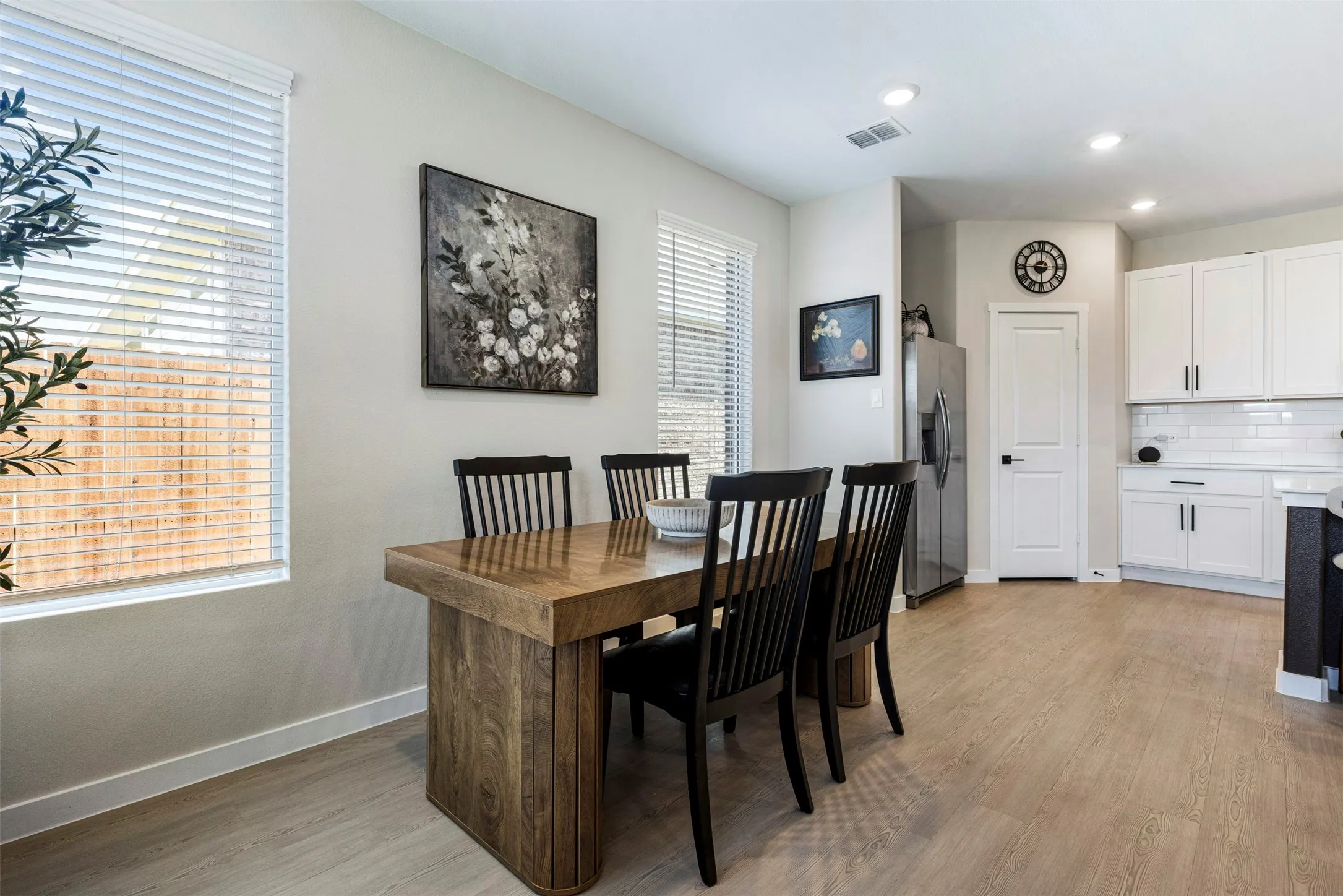Open-concept kitchen and dining area featuring wood-finish flooring, recessed lighting, white shaker cabinetry, and a subway tile backsplash