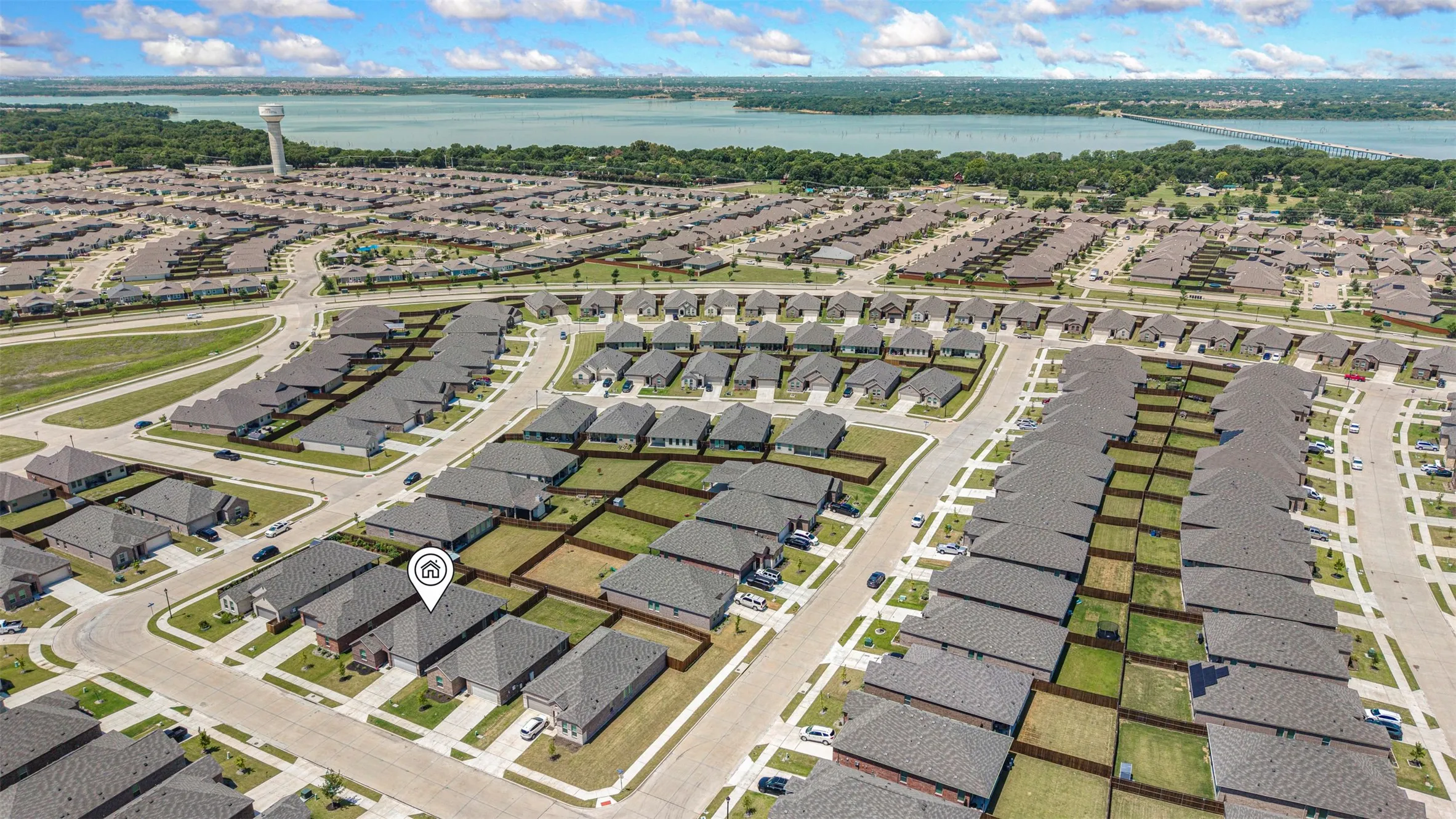 Aerial perspective showcasing an established residential development with uniform roofing, individual lot fencing, and a distant water body