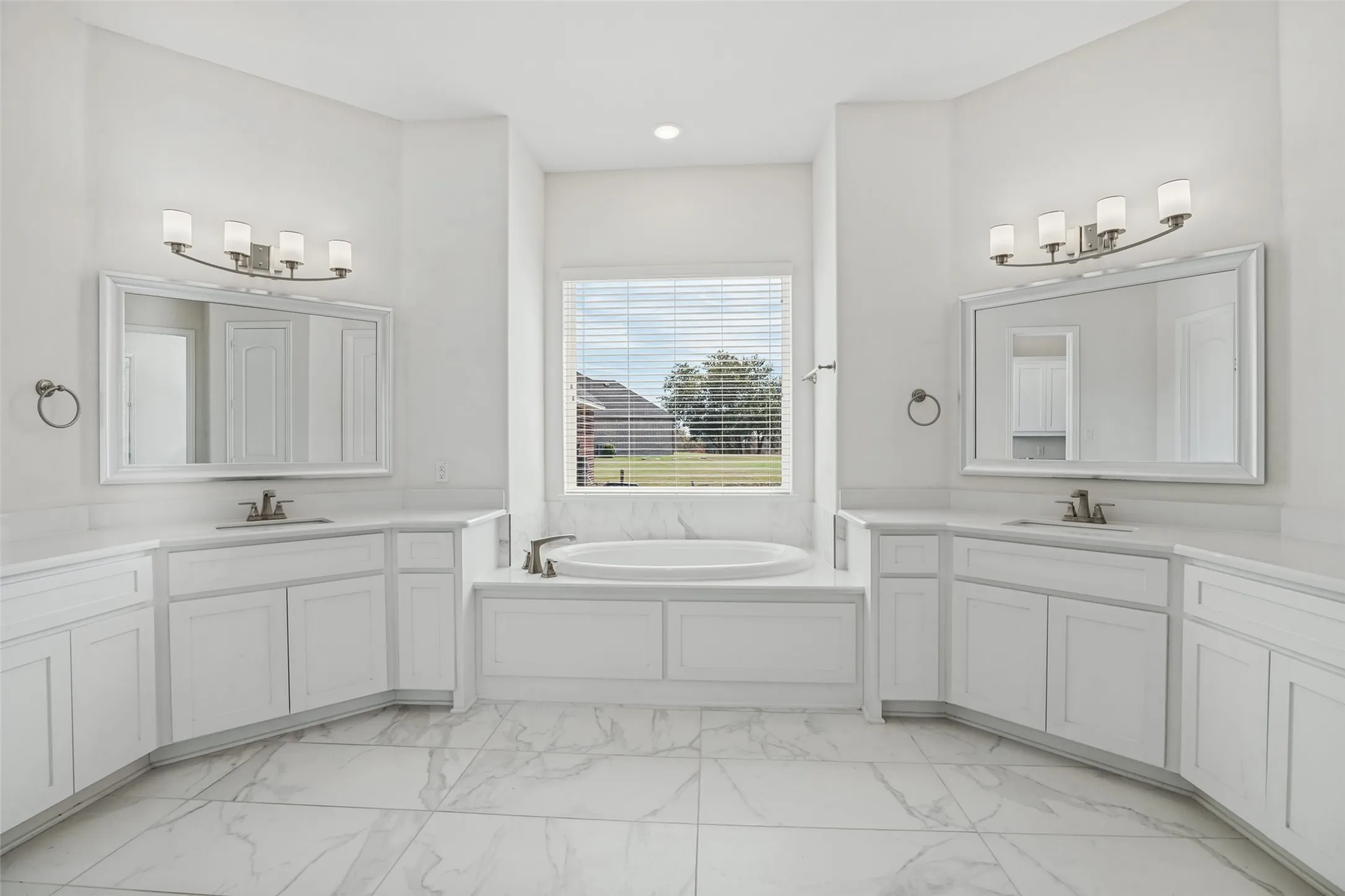 Primary bathroom with garden tub and separate vanities overlooking side yard.