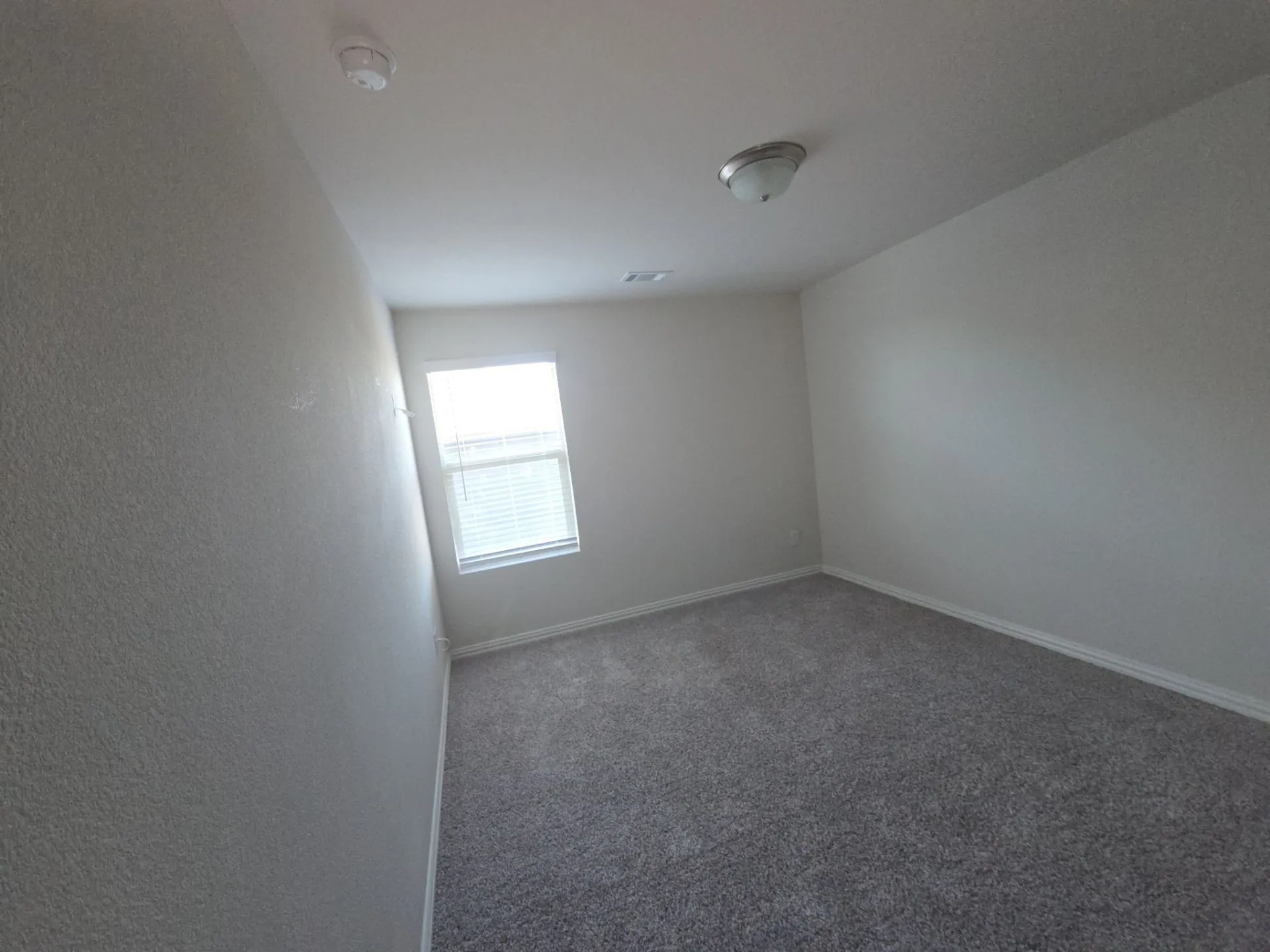Recessed window with blinds, overhead lighting, textured walls, and gray carpet flooring