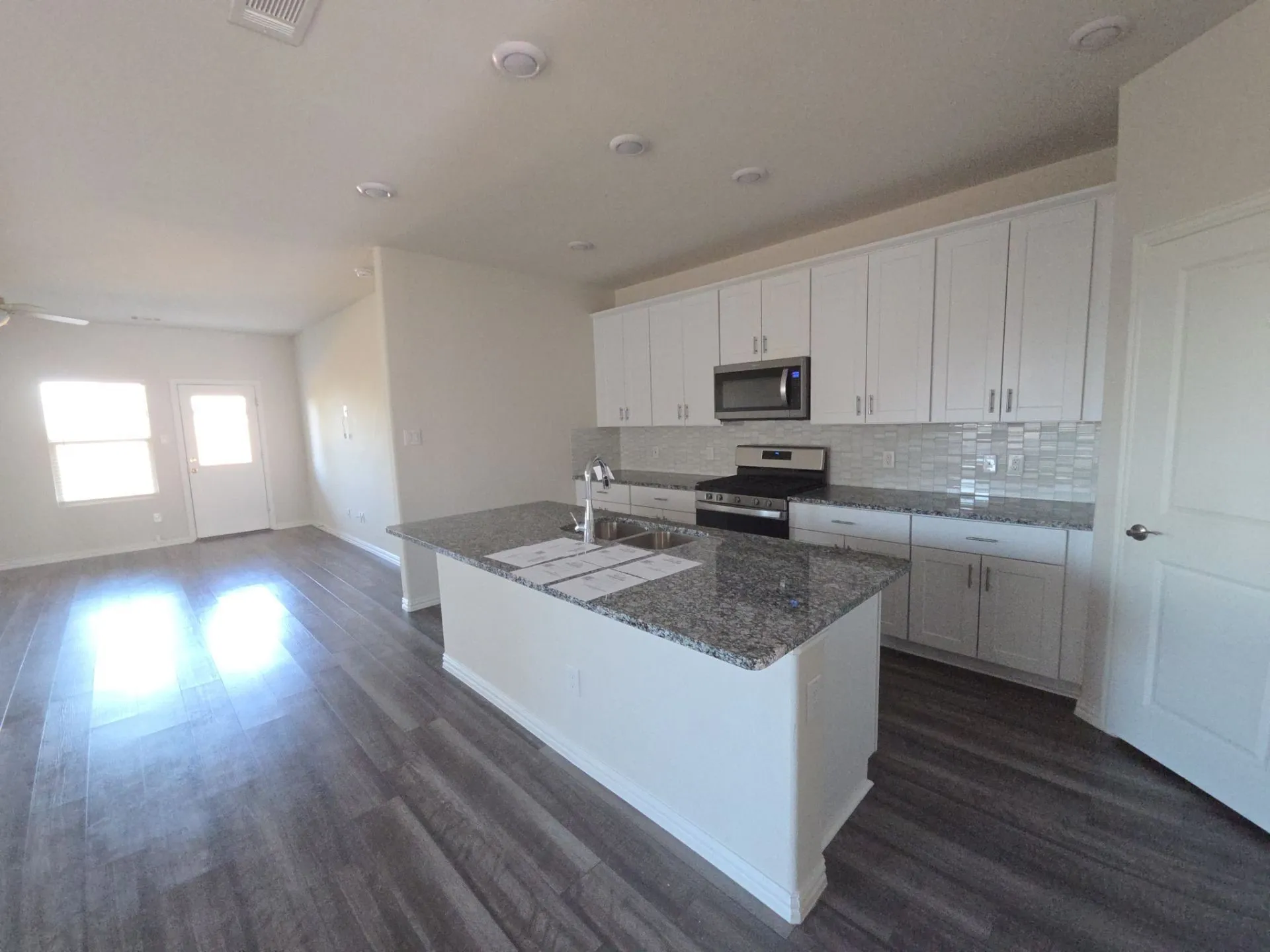 Kitchen featuring a center island with granite countertops, stainless steel appliances, white cabinetry, and a tile backsplash