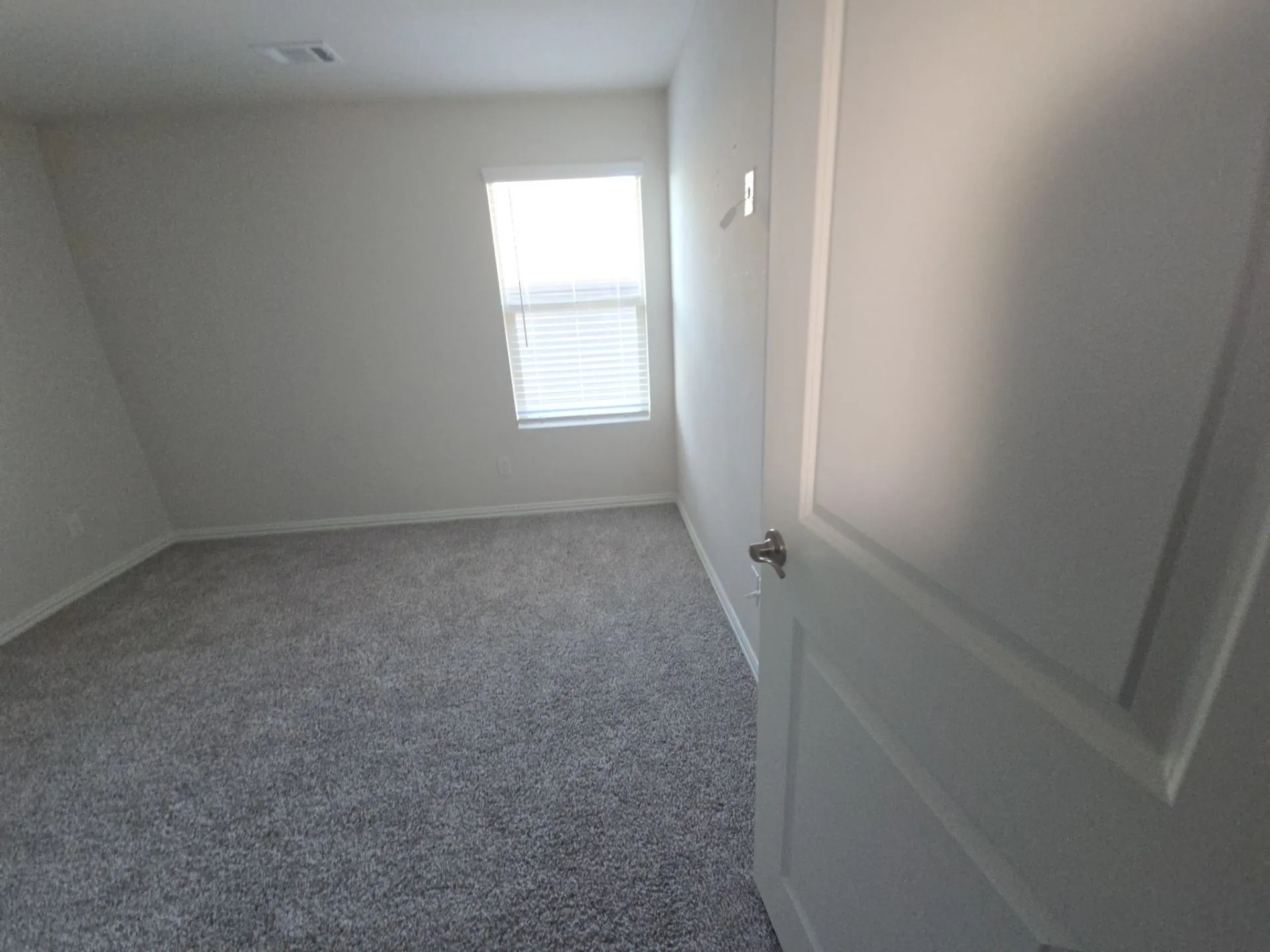 Gray carpet flooring, white painted walls, window with blinds, recessed lighting, and a white panel door