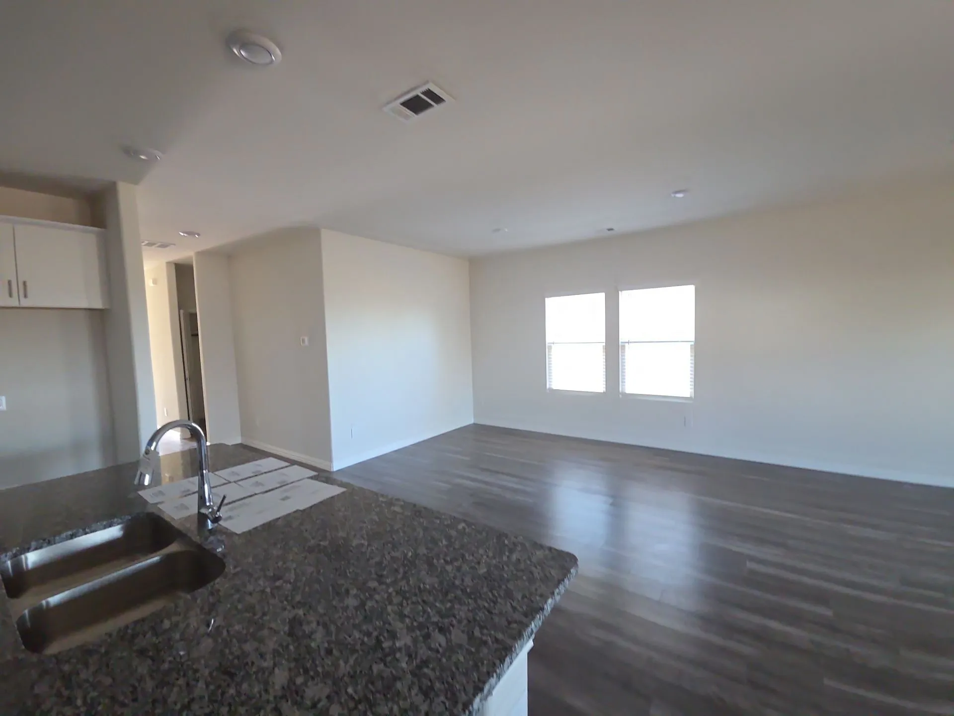 Spacious open-concept living area with dark wood-finish flooring, recessed lighting, and two windows
