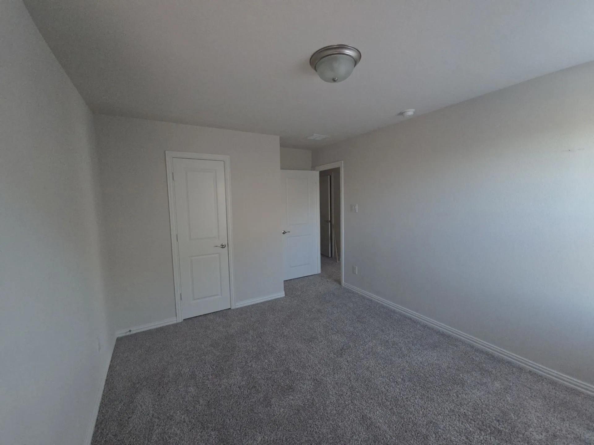 Neutral tone wall finish with a flush-mount ceiling light, white paneled doors, and grey textured carpeting