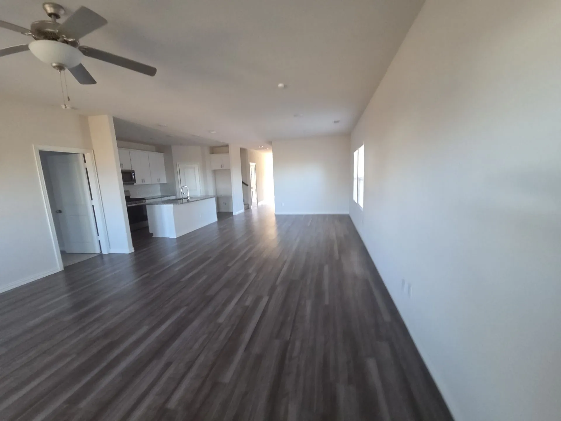 Wood-finish flooring, recessed lighting, ceiling fan, white cabinetry, kitchen island with sink