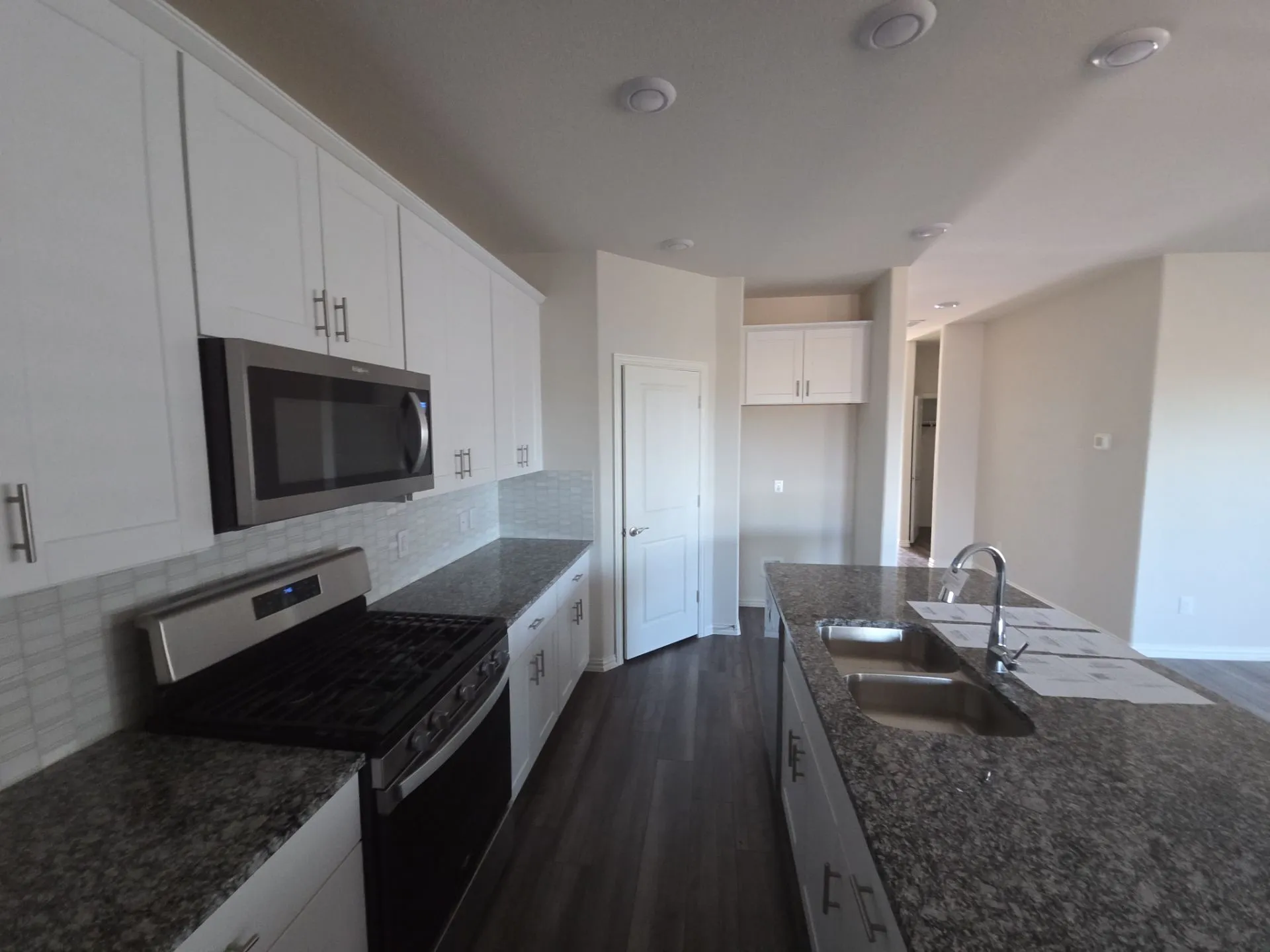 Kitchen featuring white cabinetry, granite countertops, stainless steel appliances, a tile backsplash, and dark wood-finish flooring