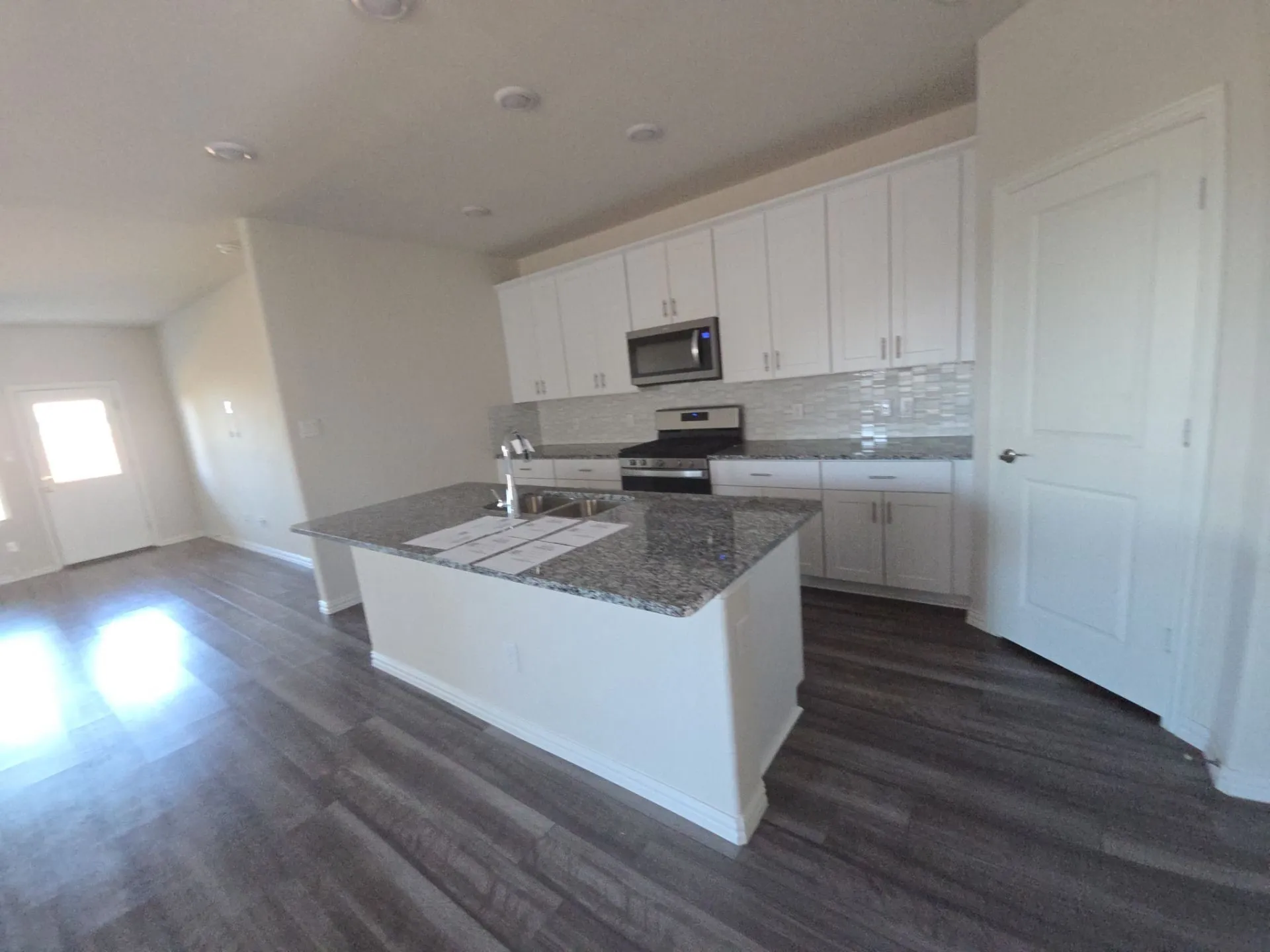 Modern kitchen featuring white cabinetry, a large island with granite countertops, stainless steel appliances, and wood-finish flooring