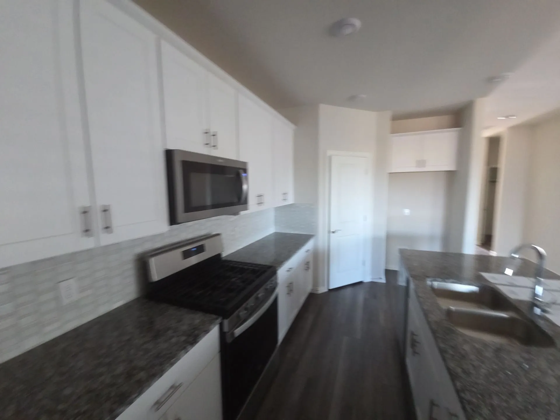 White shaker-style cabinetry, dark granite-finish countertops, stainless steel appliances, tile backsplash, and a kitchen island with an undermount sink