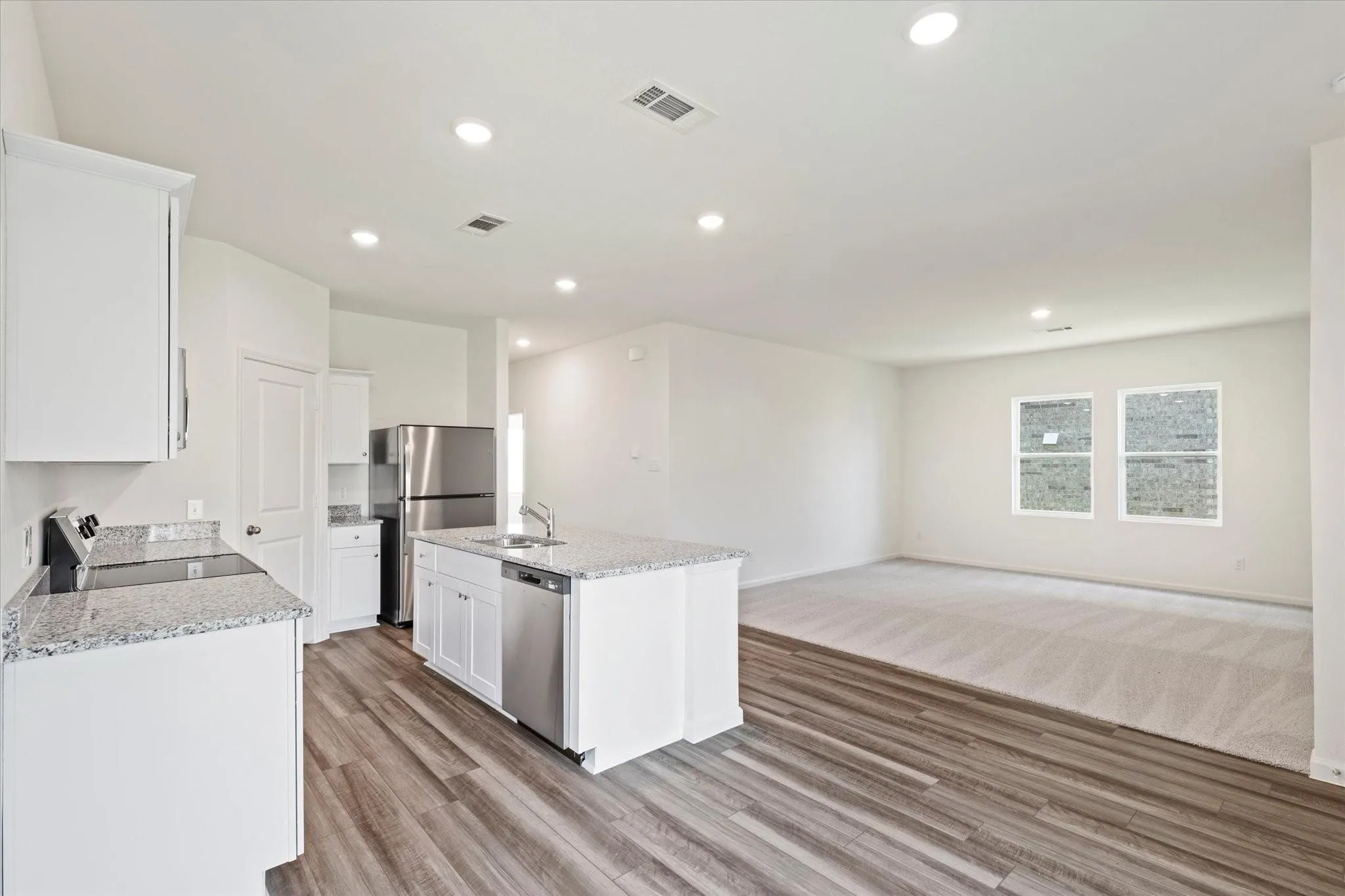 Kitchen featuring an island with sink, stainless steel appliances, white cabinetry, granite countertops, and wood-finish flooring