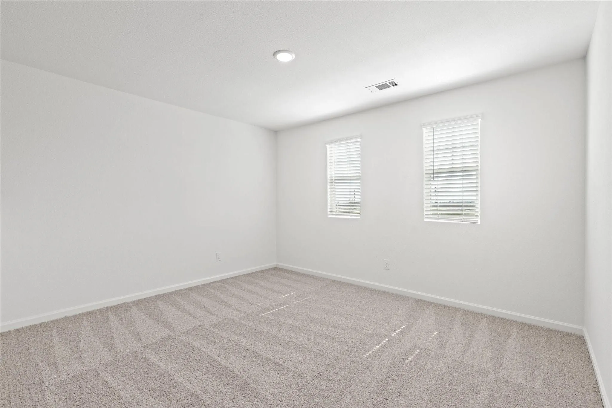Neutral tone wall color, recessed ceiling lighting, light-toned patterned carpet, multiple windows with blinds