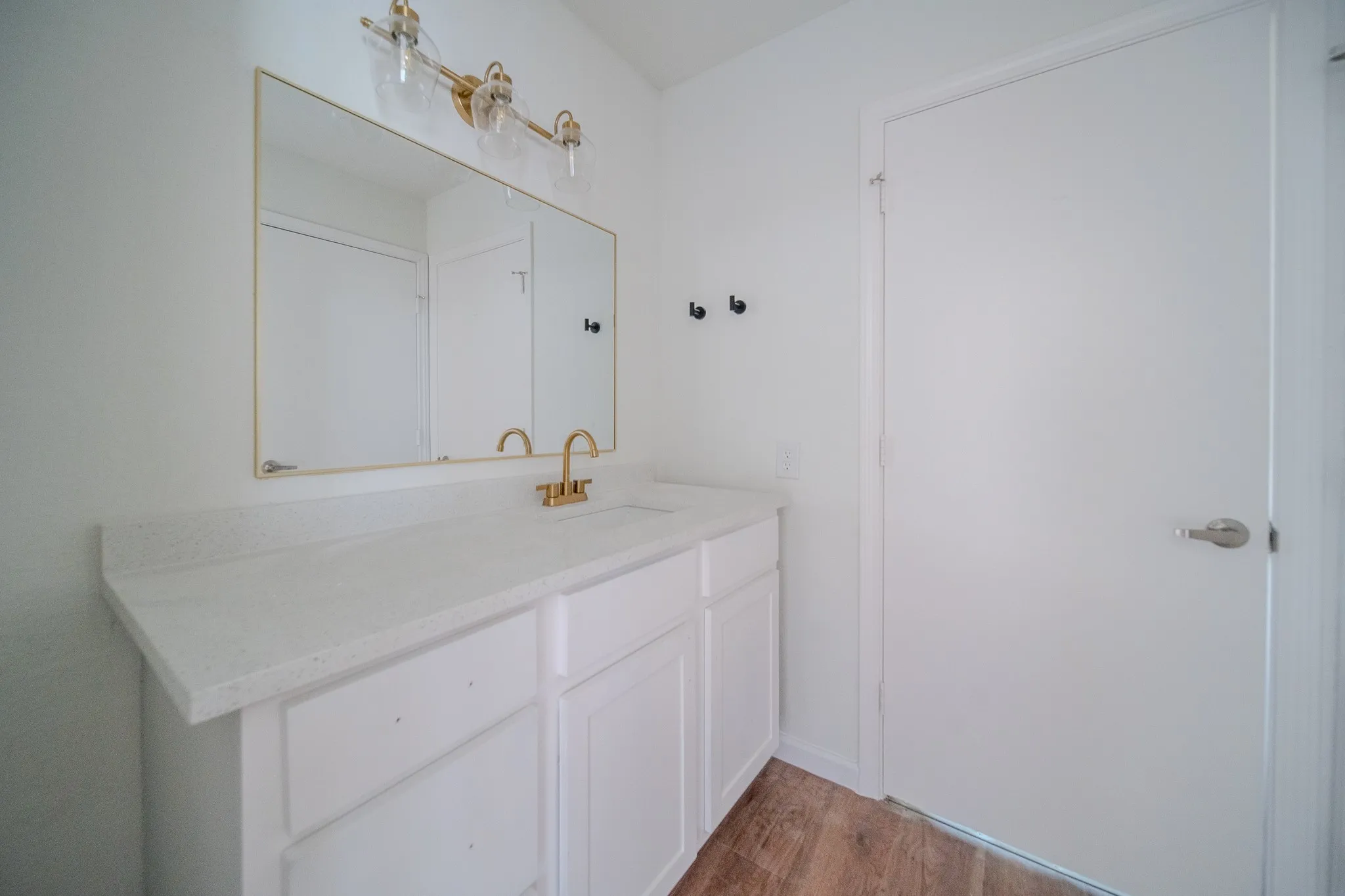 White vanity with a light-toned countertop, gold-finish hardware, and wood-finish flooring