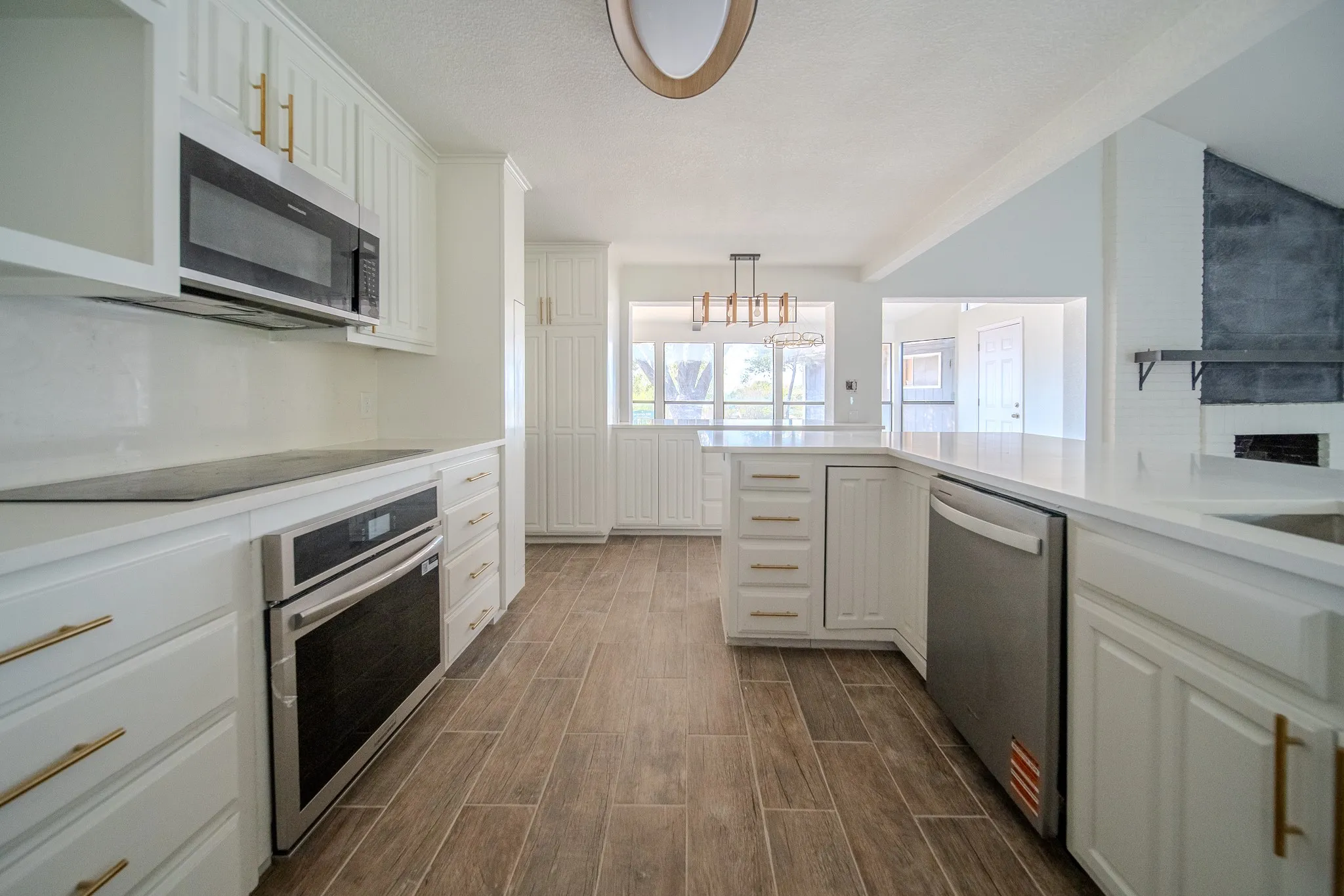 White cabinetry with gold-finish hardware, stainless steel appliances, white countertops, wood-finish flooring, and a built-in oven