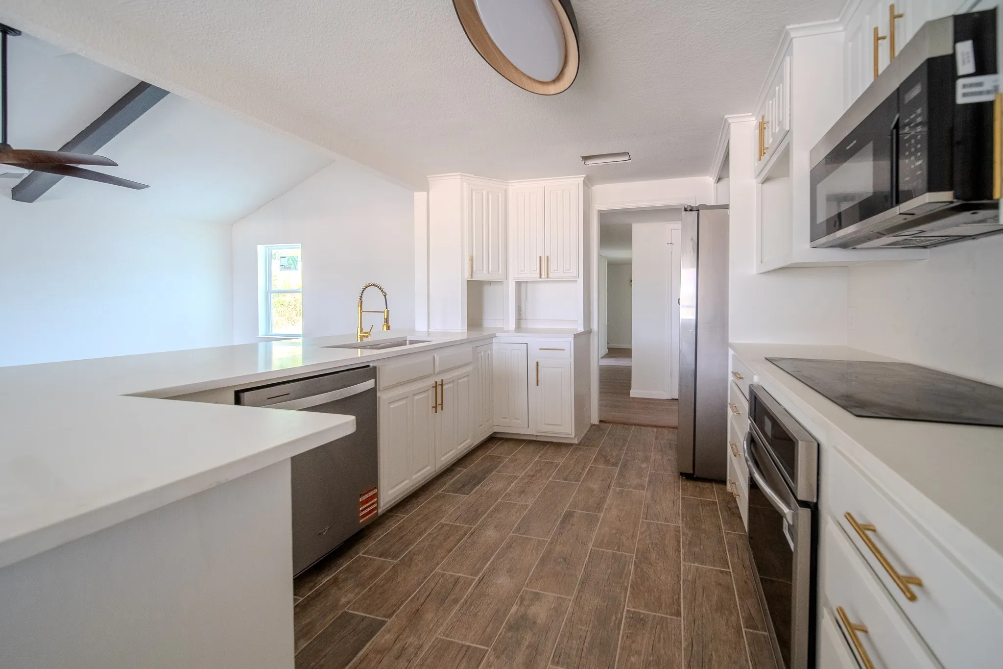 Modern kitchen featuring white cabinetry, stainless steel appliances, wood-finish flooring, white countertops, and a gold-finish faucet