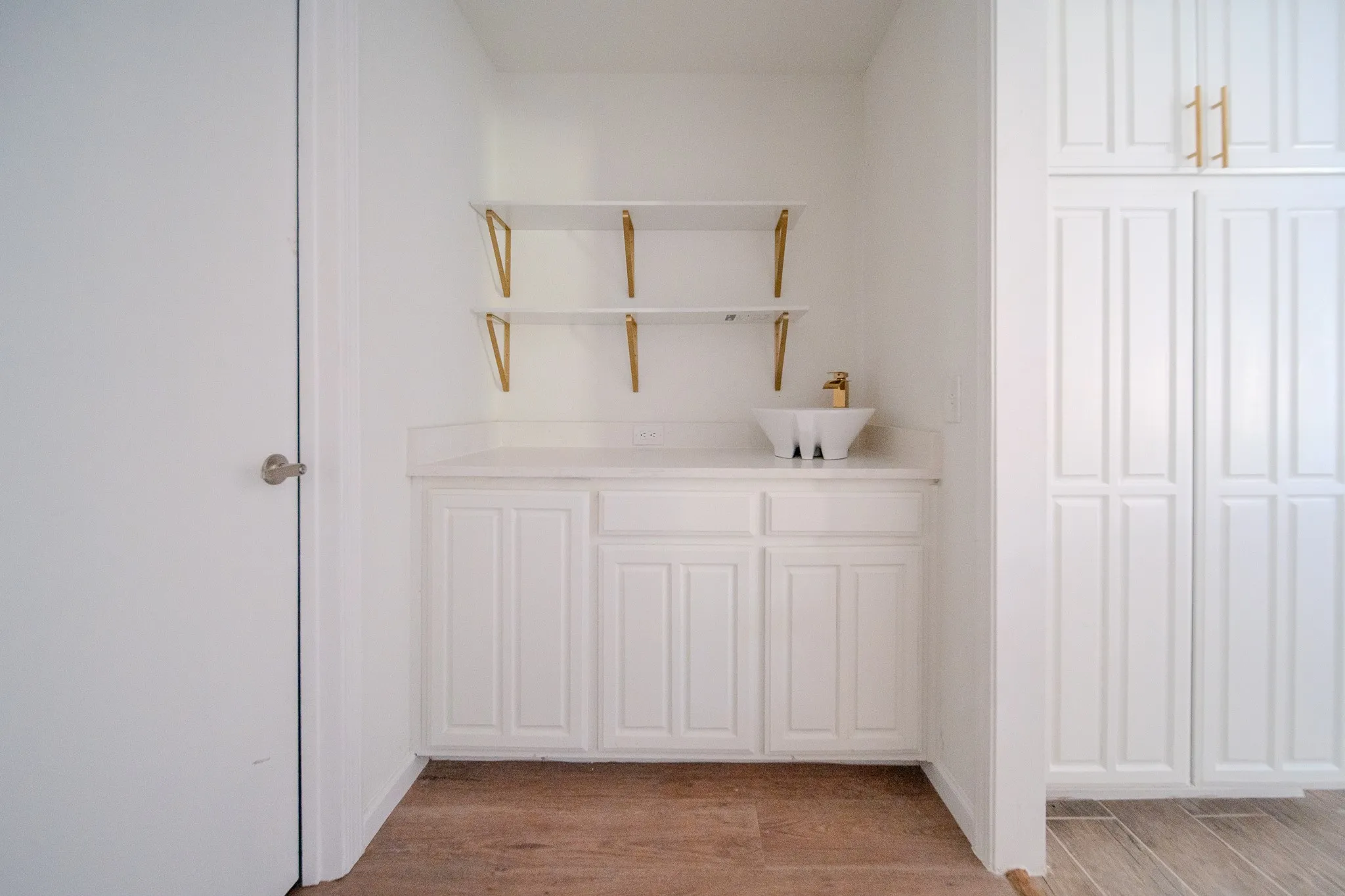 White cabinetry with gold-tone hardware, a white vessel sink, and an integrated countertop