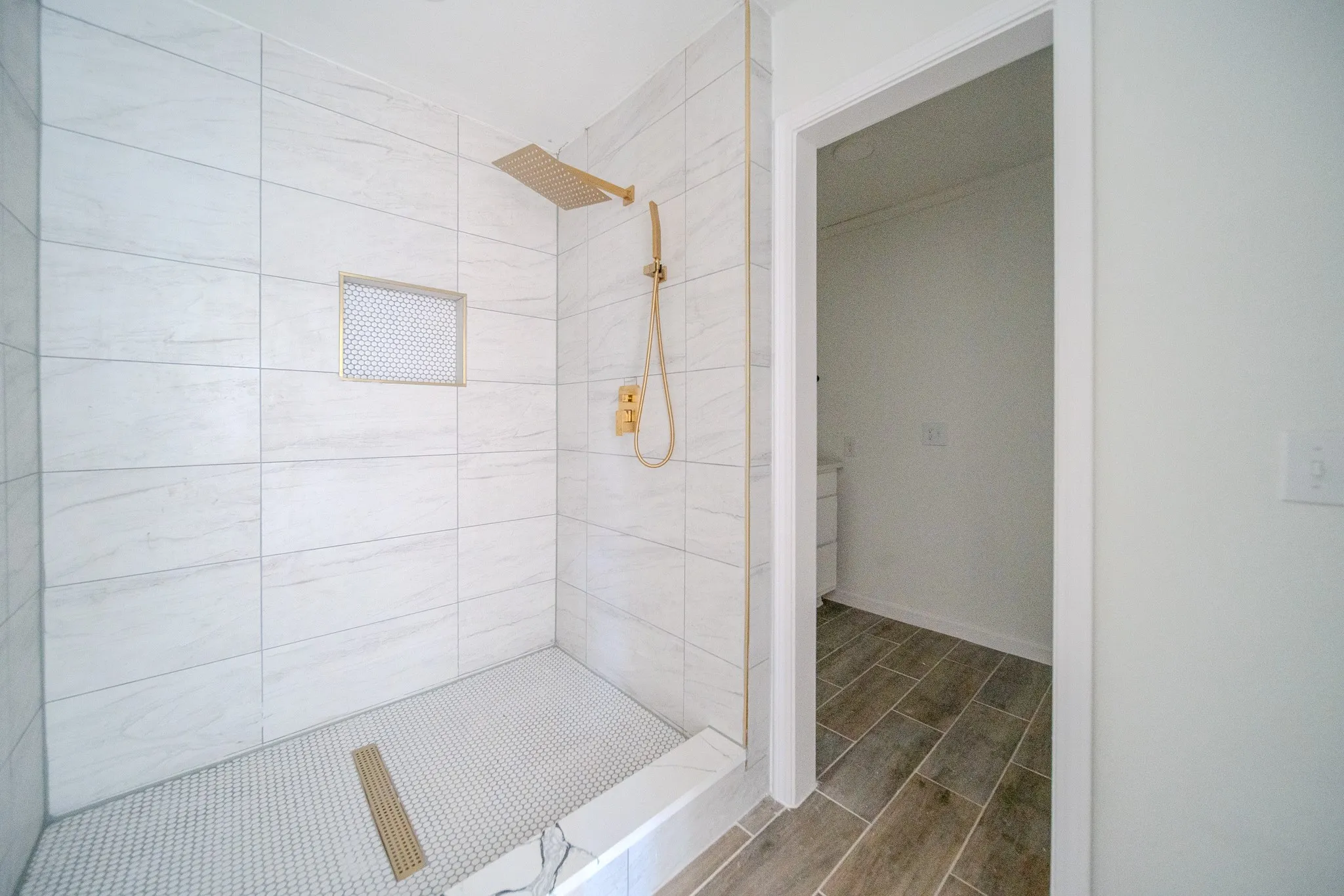 Walk-in shower with large format wall tiles, penny tile floor, recessed niche, and gold-finish fixtures