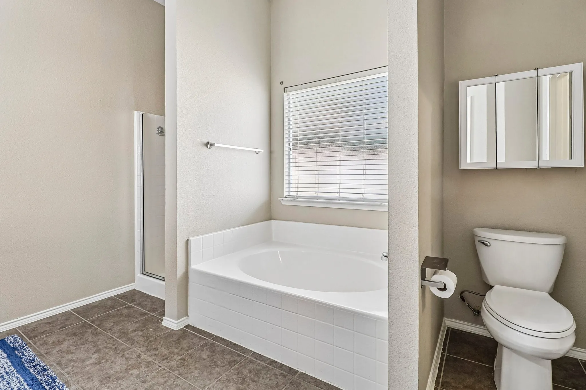 Soaking tub with white tile surround, privacy window with blinds, enclosed shower, and tri-fold medicine cabinet