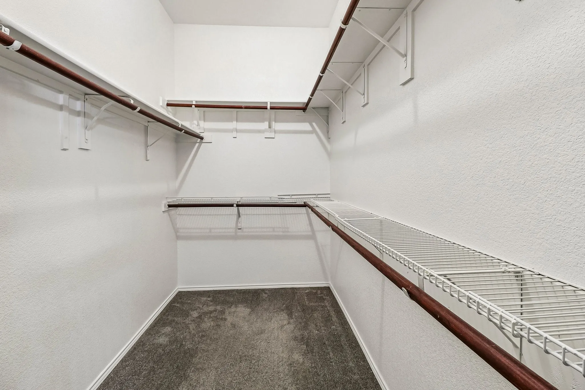 Walk-in closet featuring white wire shelving, wood-finish hanging rods, and neutral-toned carpeting