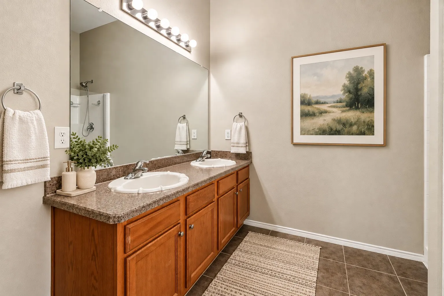 Dual vanity with integrated sinks, wood-finish cabinetry, a large wall-mounted mirror, and tile flooring