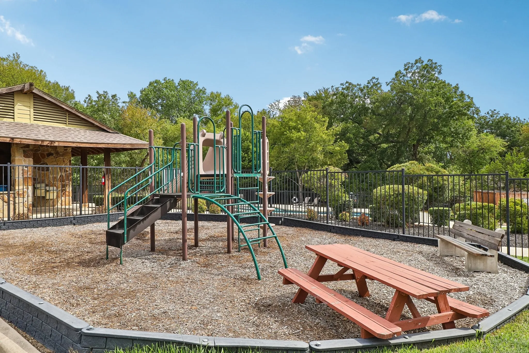 Recreational area featuring a playground structure with slides and stairs, a picnic table, and a built-in stone bench
