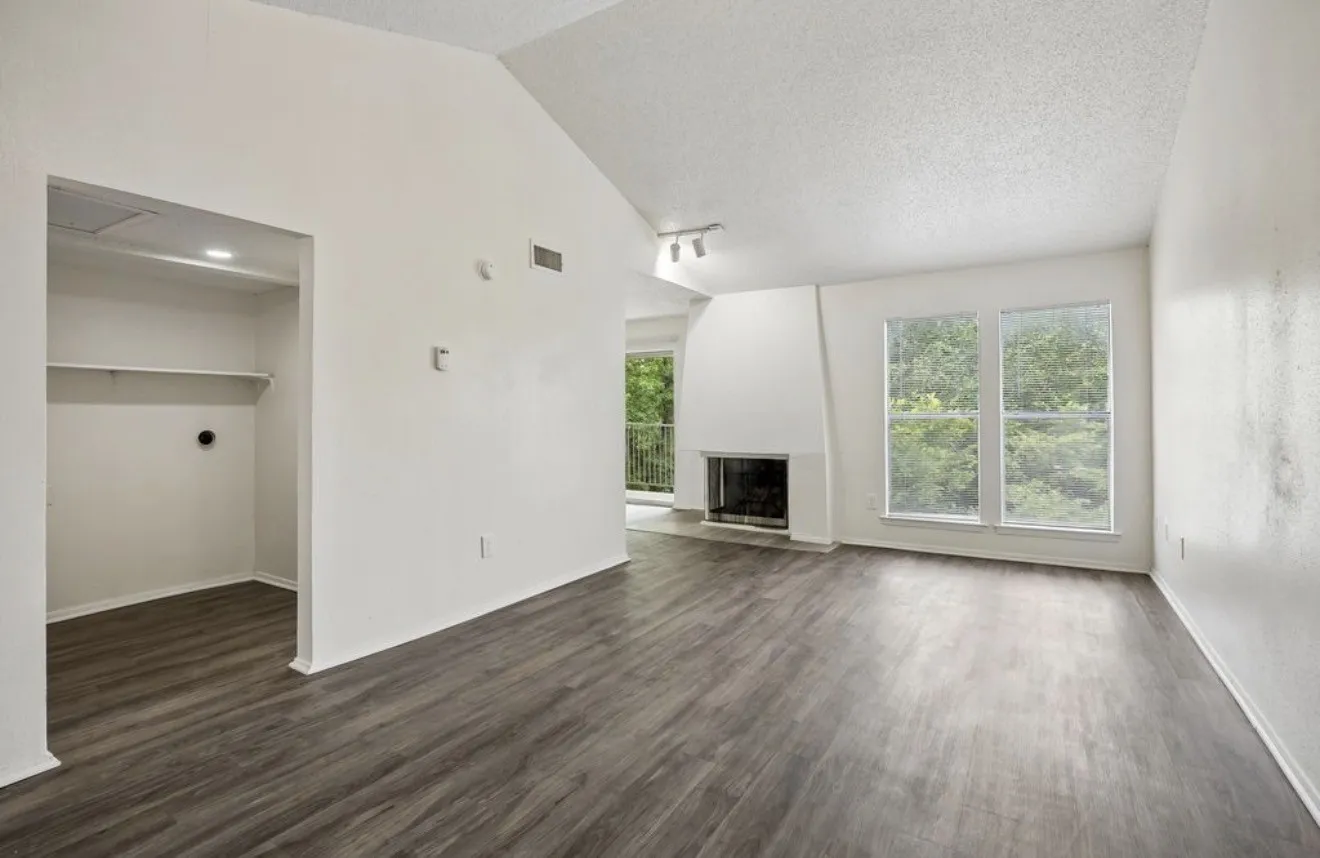 Vaulted ceiling, wood-finish flooring, two large windows, fireplace, and a built-in storage area