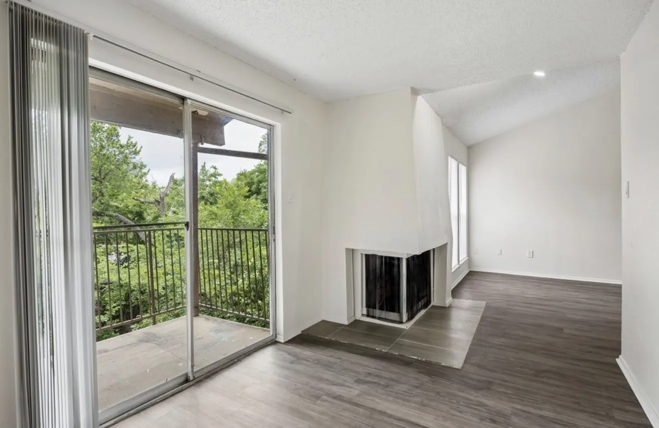 Sliding glass door opening to a private balcony with metal railings, wood-finish flooring, a fireplace with hearth, and a vaulted ceiling