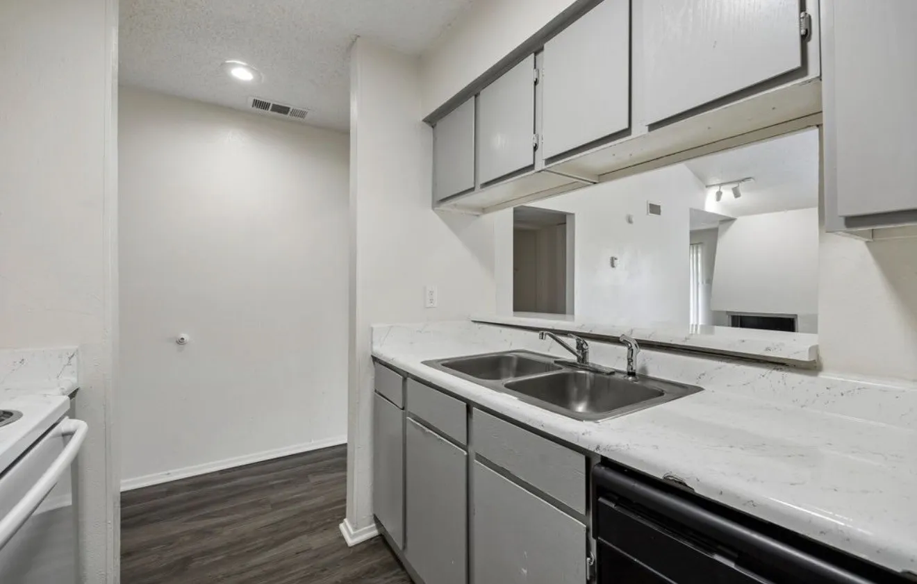 Kitchen featuring a double basin stainless steel sink, pass-through window, wood-finish flooring, white countertops, and gray cabinetry