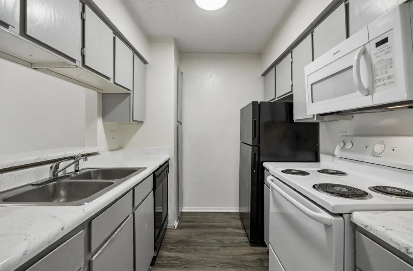 Galley kitchen featuring wood-finish flooring, white countertops, dual basin sink, gray cabinetry, and white appliances