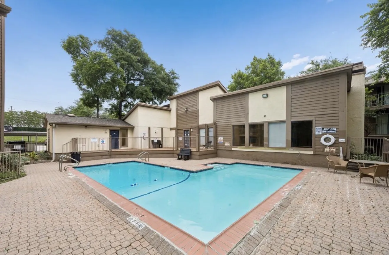 Community swimming pool with a brick coping and perimeter paving, surrounded by a wood deck and mature trees