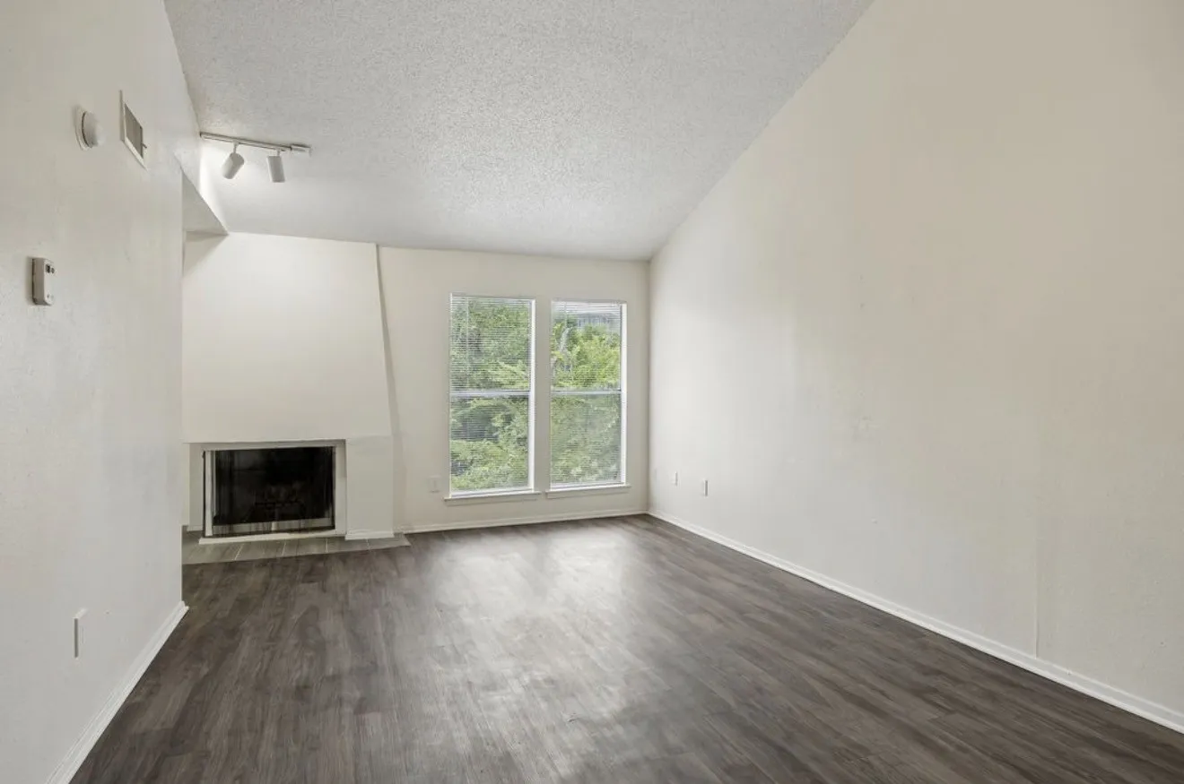 Vaulted ceiling with track lighting, multiple windows, built-in fireplace, and wood-finish flooring