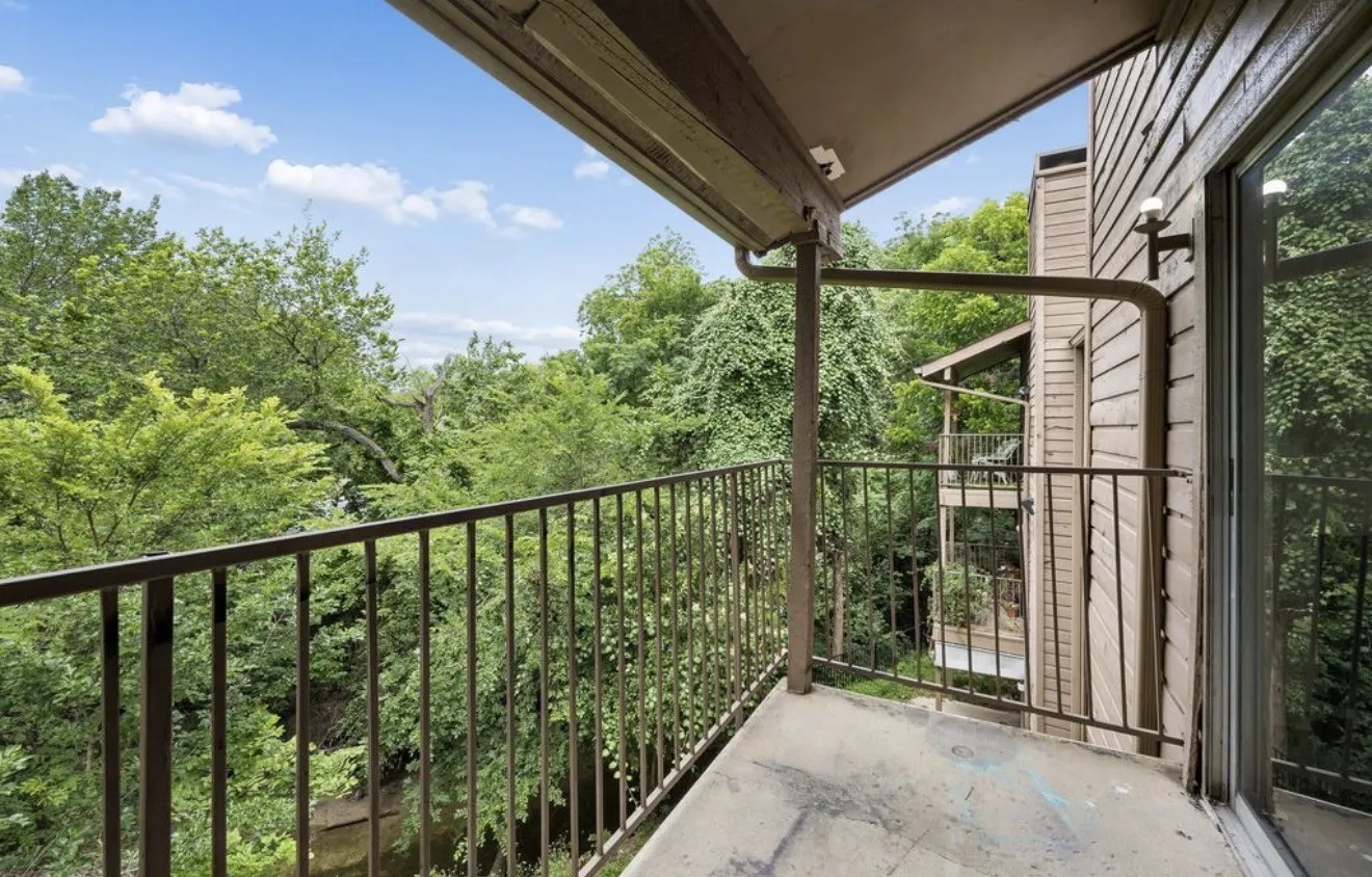 Private balcony with a metal railing and mature tree scenery