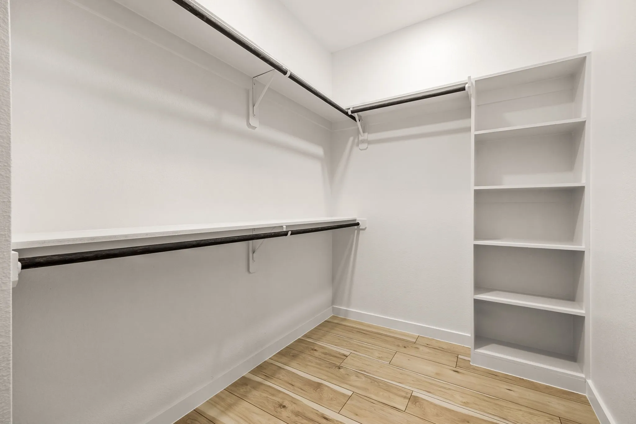 Walk-in closet featuring wood-finish flooring, built-in shelving, and multiple hanging rods