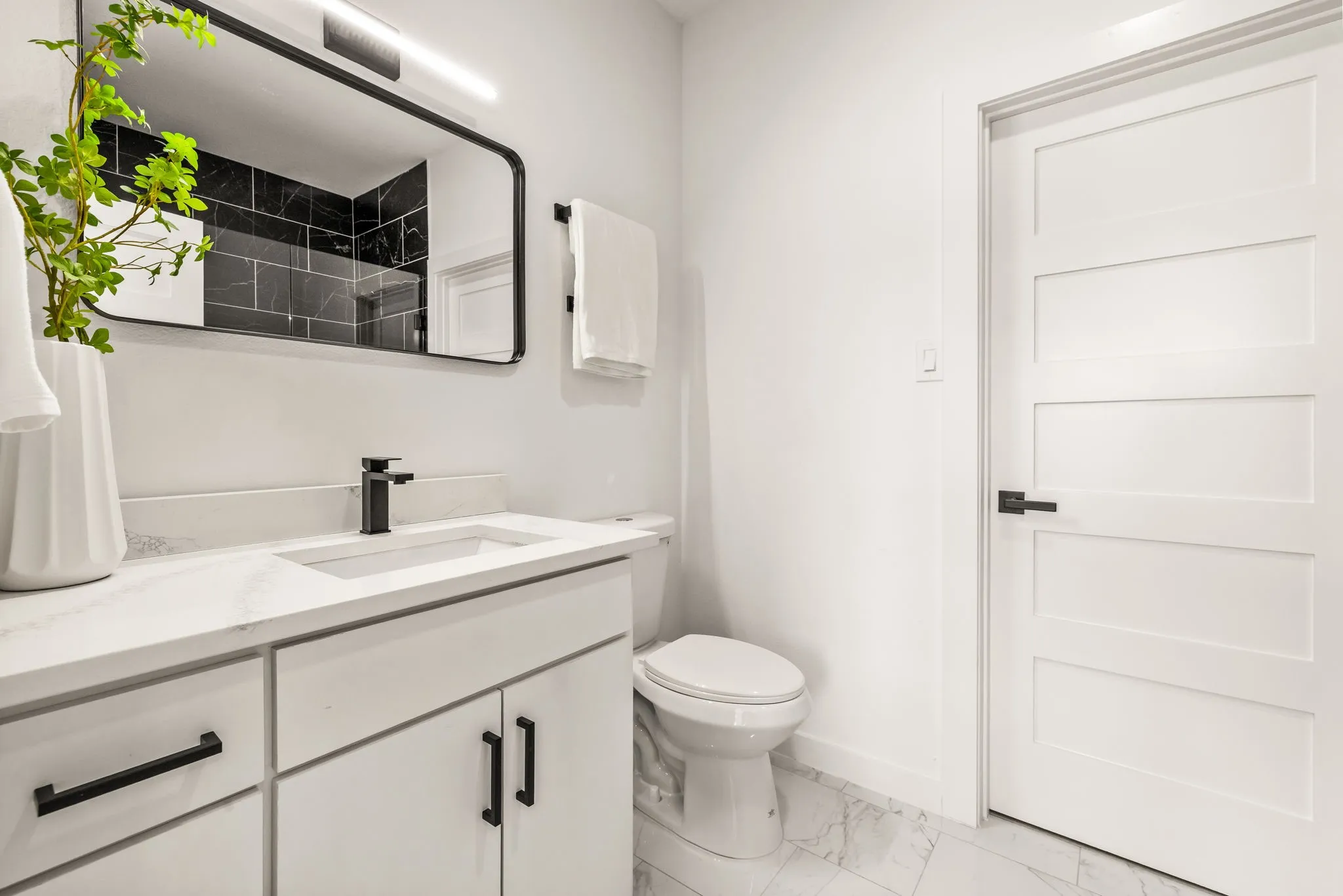 White vanity with a single basin, dark-finish faucet, and a large wall mirror