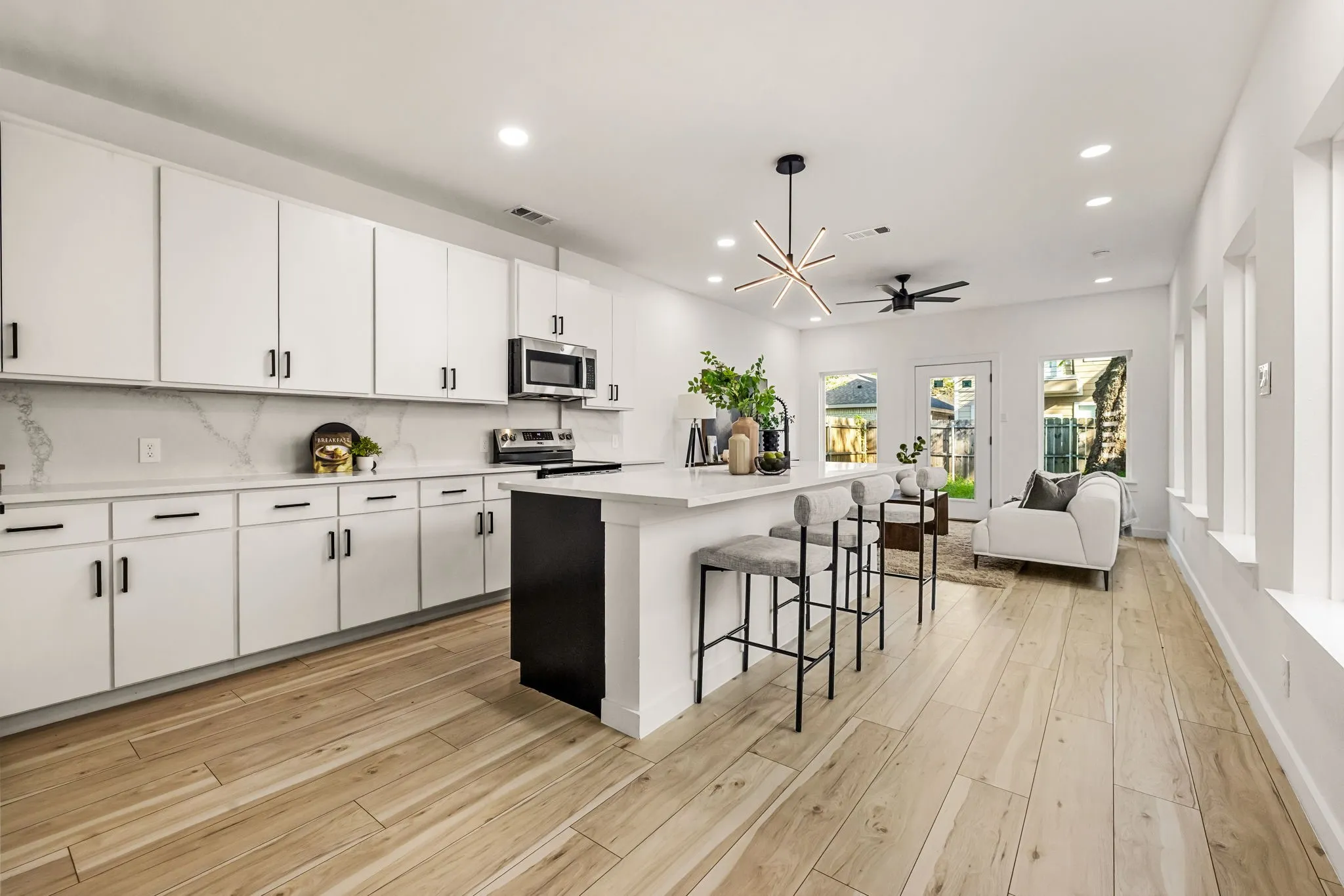 Open-concept living space with light wood-finish flooring, white cabinetry, and a kitchen island with seating