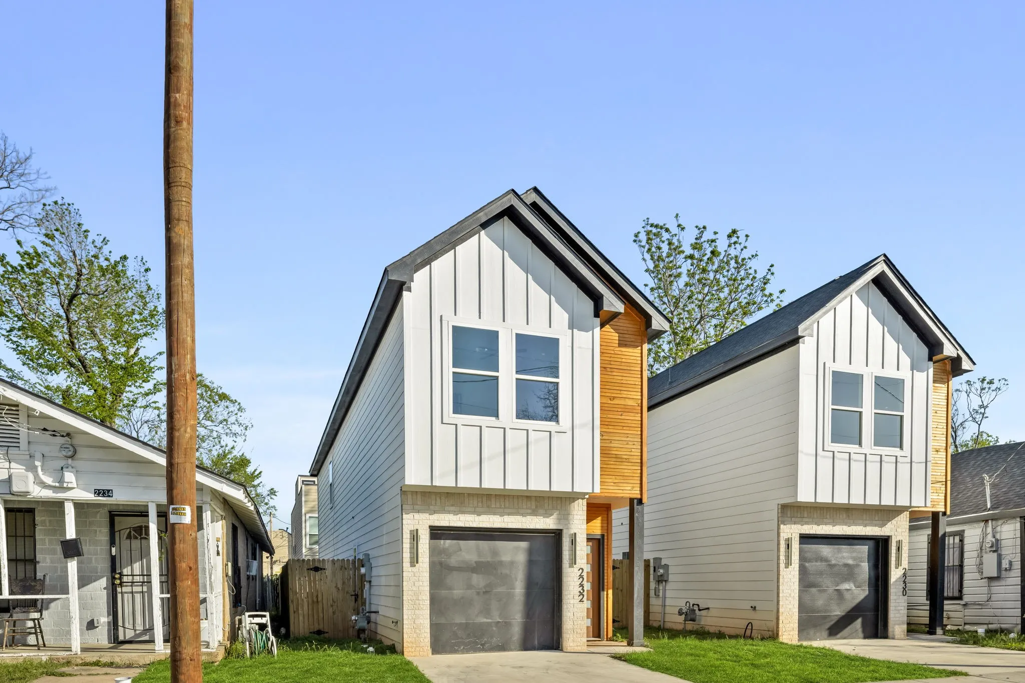 Modern exterior with vertical white siding, natural wood-finish accents, a black asphalt shingle roof, and an integrated garage