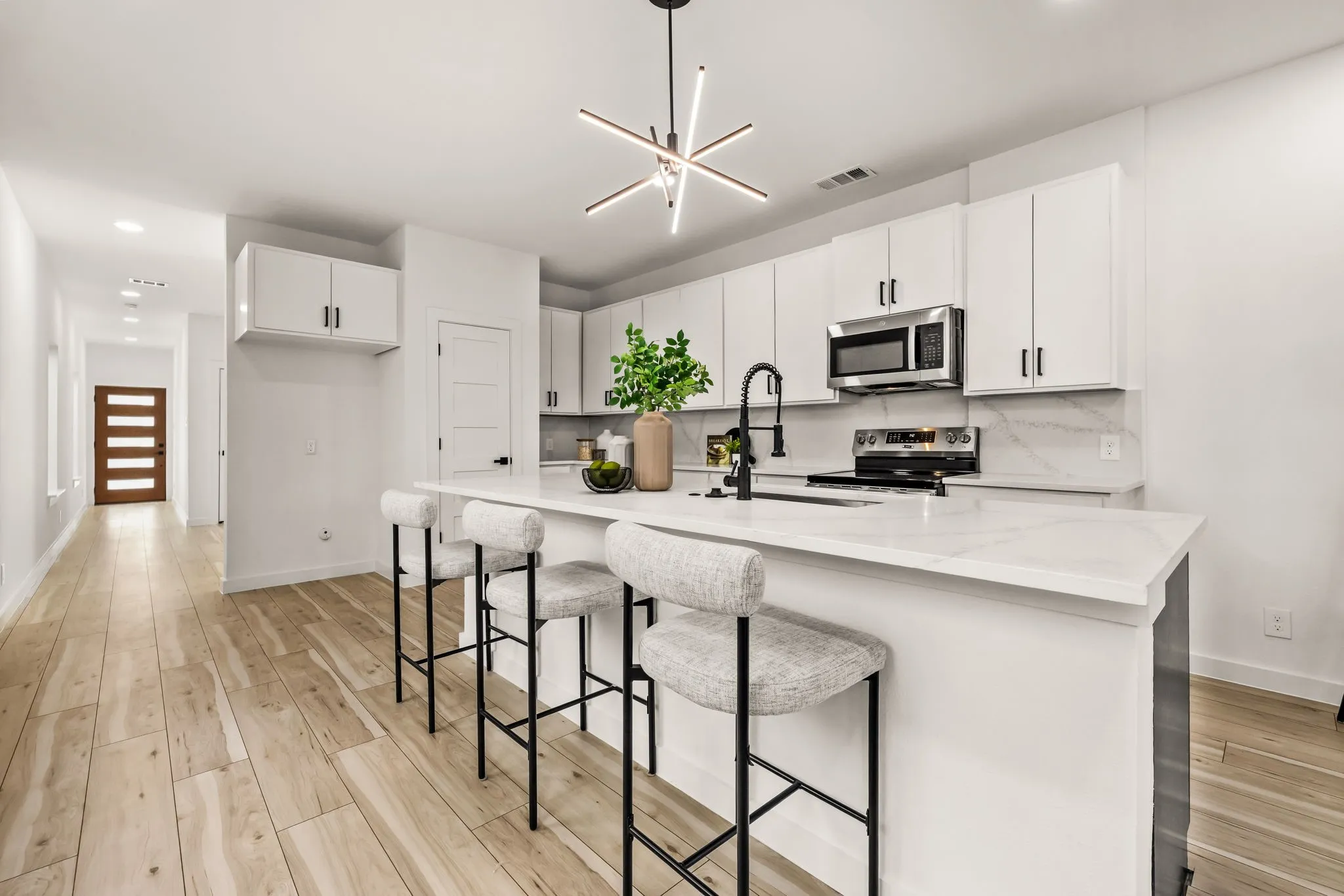 Contemporary kitchen featuring white cabinetry, stainless steel appliances, a white island with countertop seating, a black faucet, and a modern linear chandelier