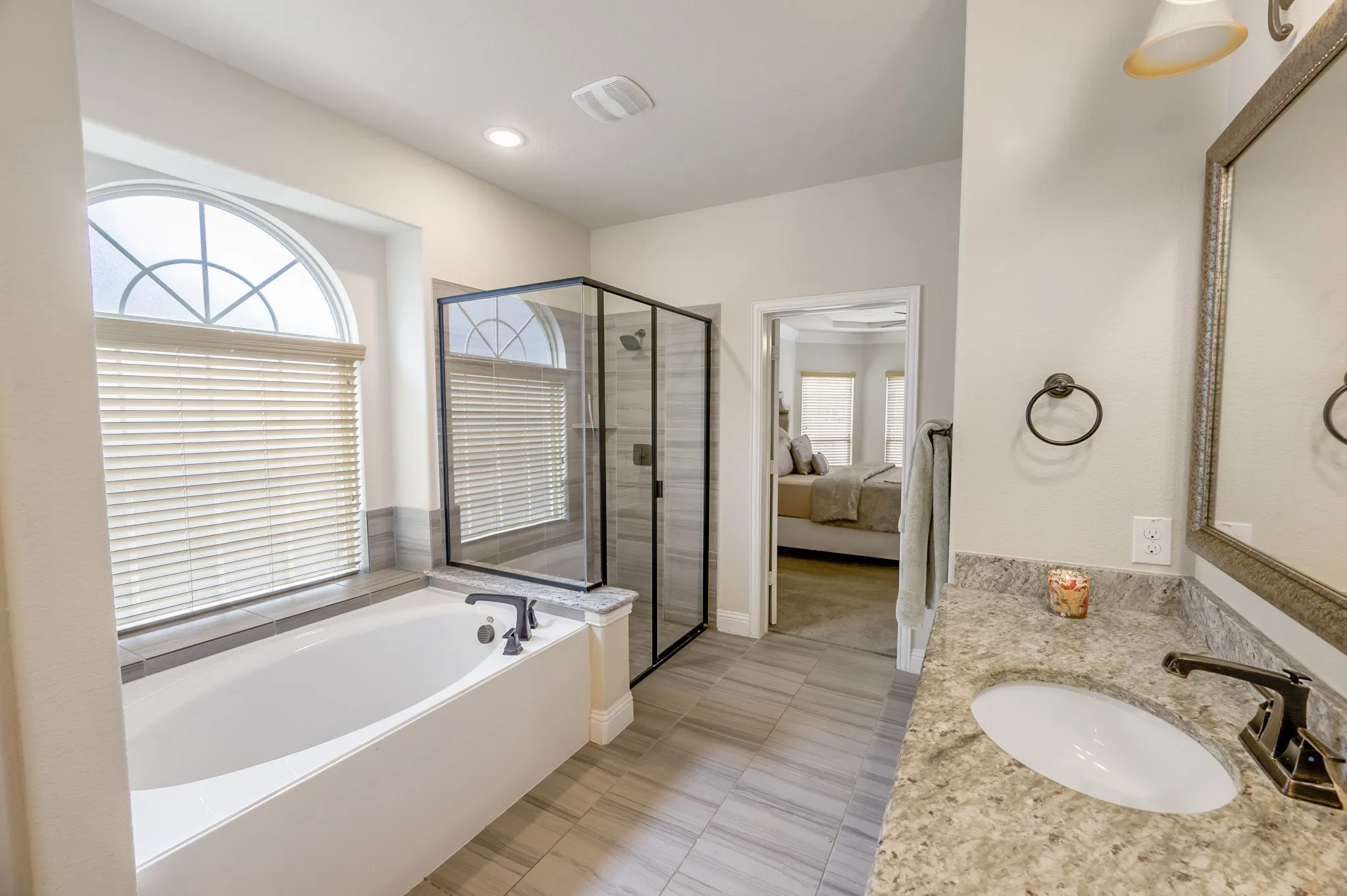 Dual sink vanity with stone countertop, walk-in shower with glass enclosure, soaking tub, and arched window