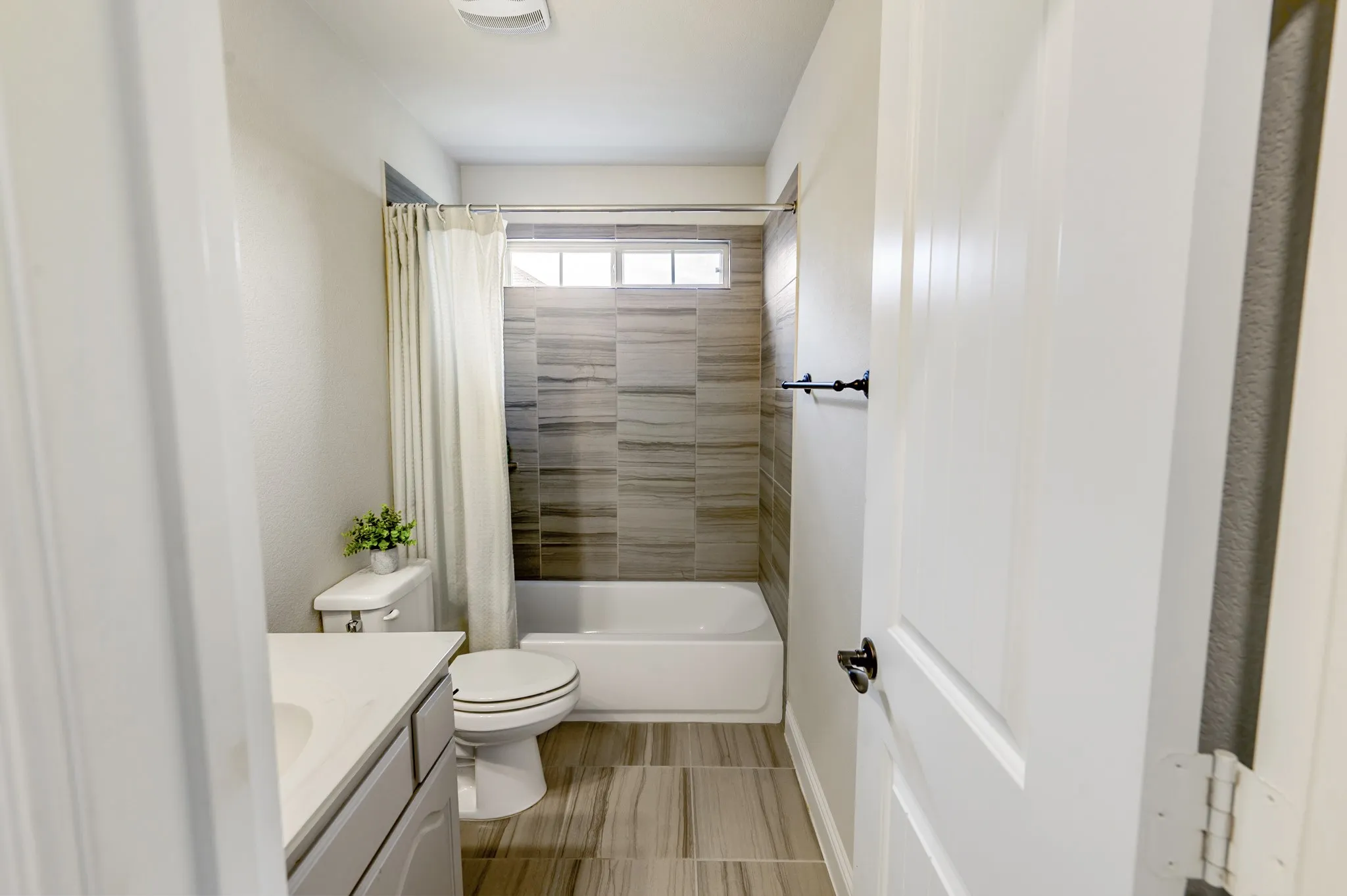 Bathtub with tile surround, high transom window, and tile flooring