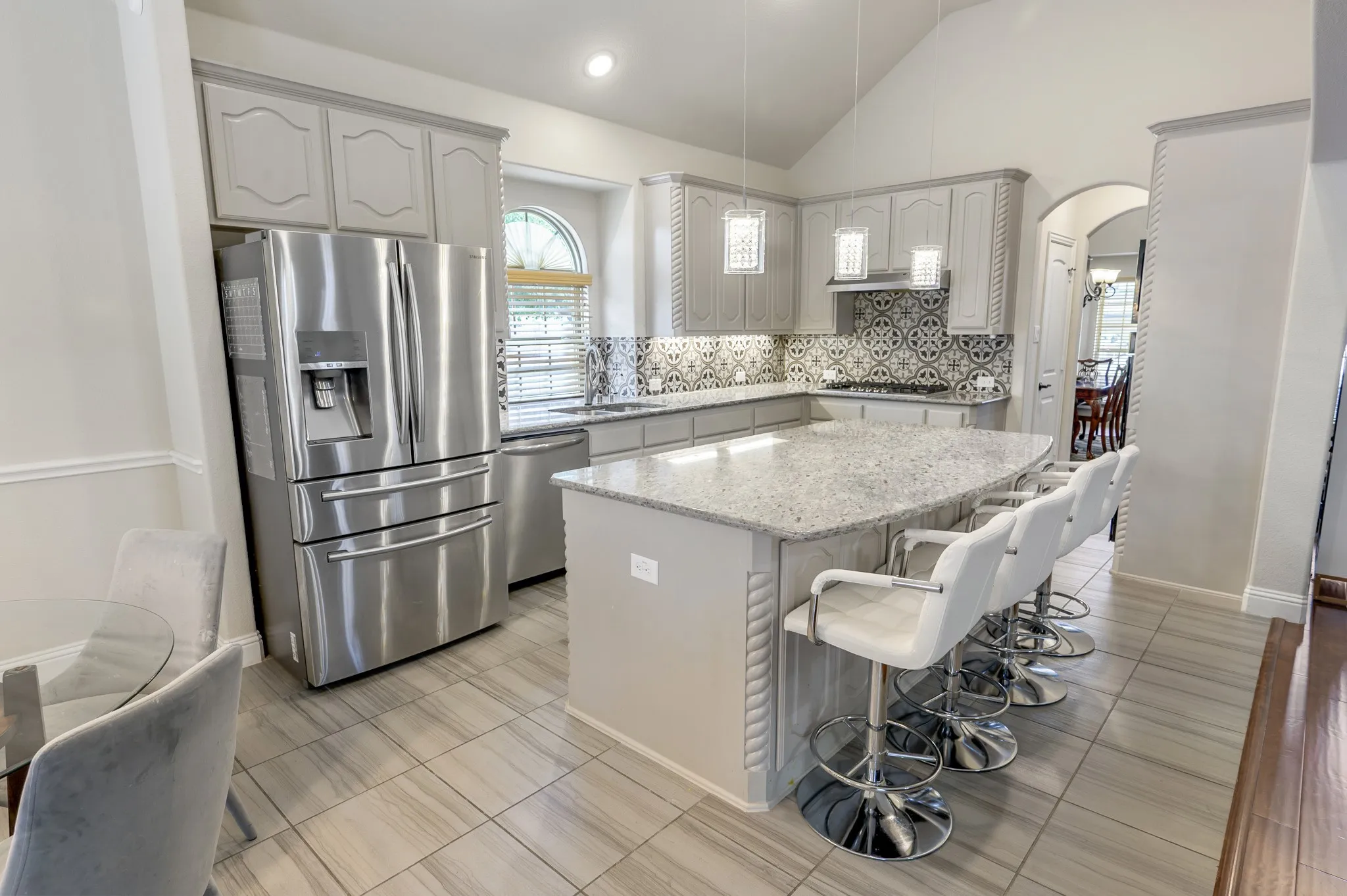Kitchen featuring a vaulted ceiling, light gray cabinetry, stainless steel appliances, a patterned tile backsplash, and an island with a light-colored countertop