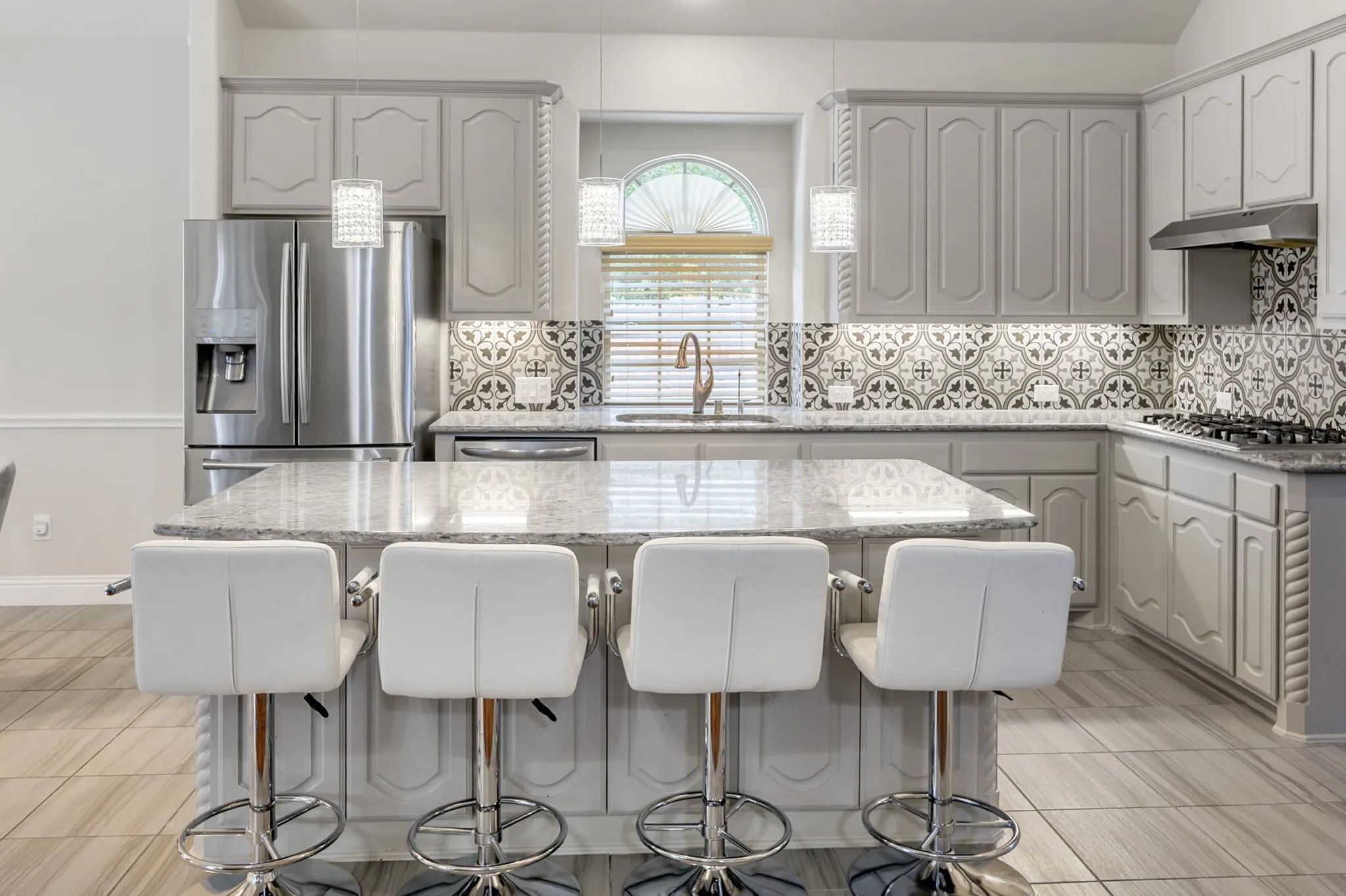 Kitchen featuring a center island with seating, patterned tile backsplash, stainless steel appliances, pendant lighting, and light-toned cabinetry