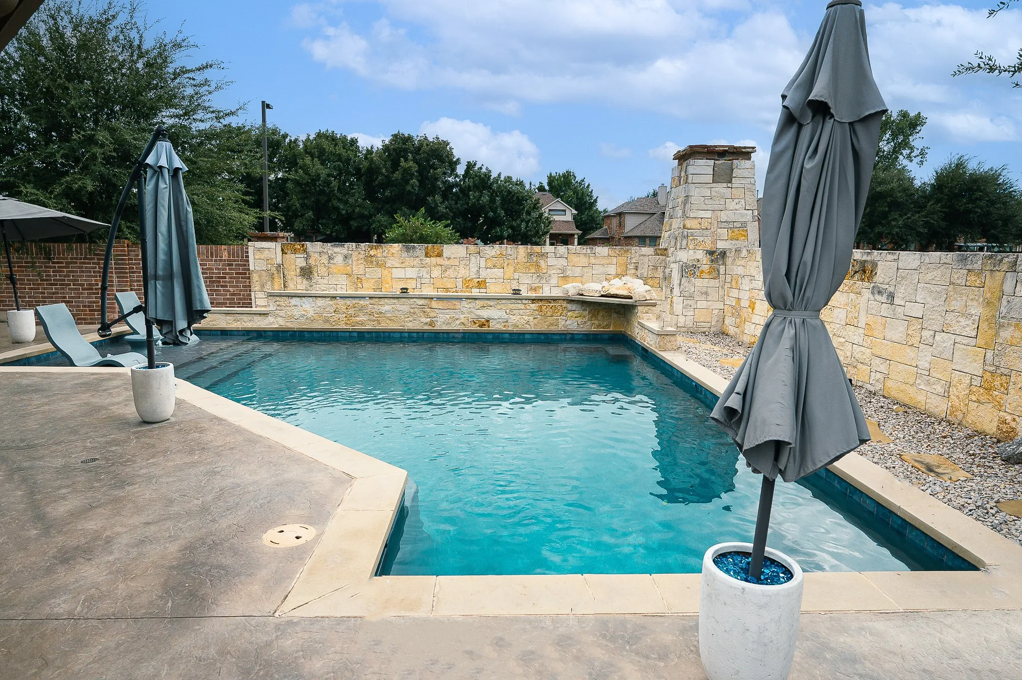 In-ground swimming pool featuring a stone surround, integrated water feature, and a paved patio